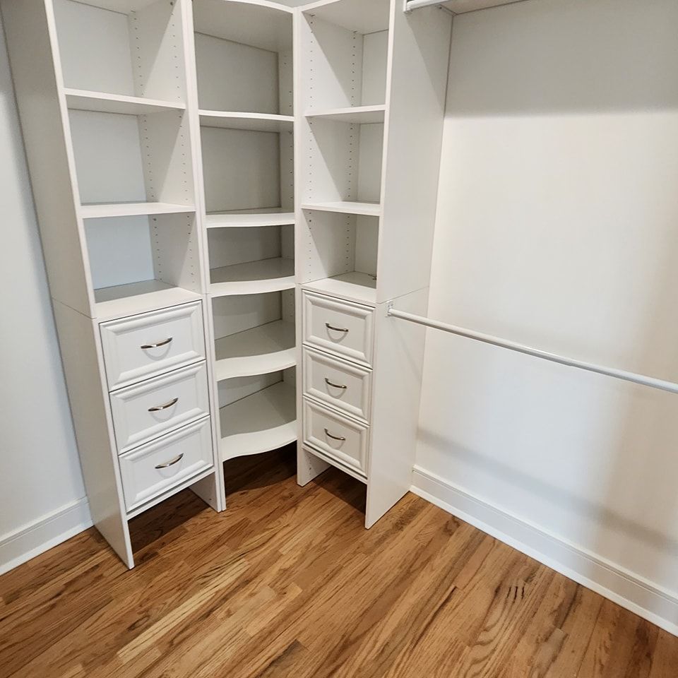 A walk in closet with hardwood floors and white shelves and drawers.