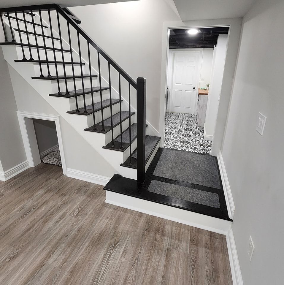 A staircase in a basement with wooden floors and a black railing.