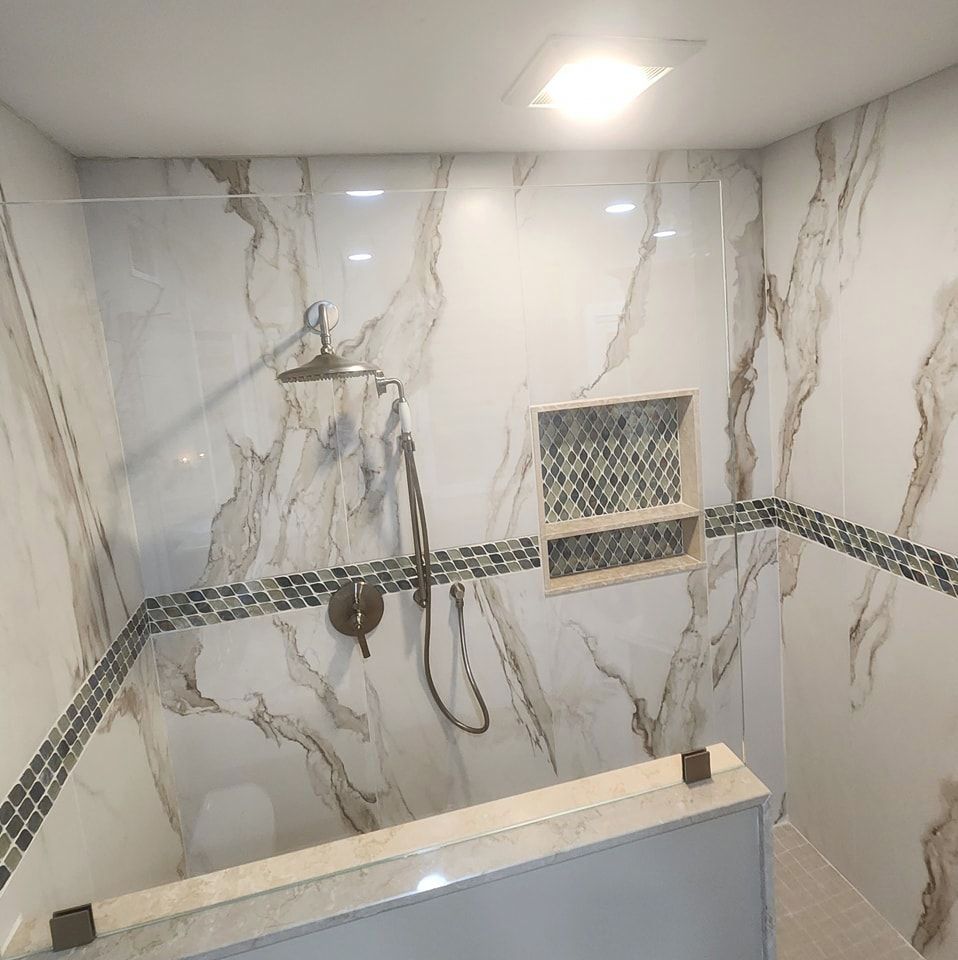 A bathroom with marble walls and a walk-in shower with a glass door.