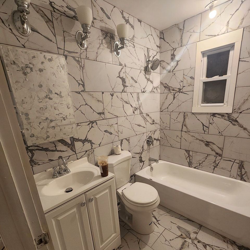 A bathroom with marble tiles, a toilet, sink, and bathtub