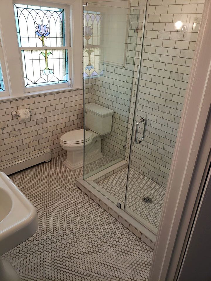 A bathroom with a toilet, sink, shower, and stained glass window