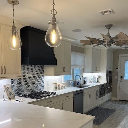 A kitchen with white cabinets, a stove, a sink, pendant lights, and a ceiling fan