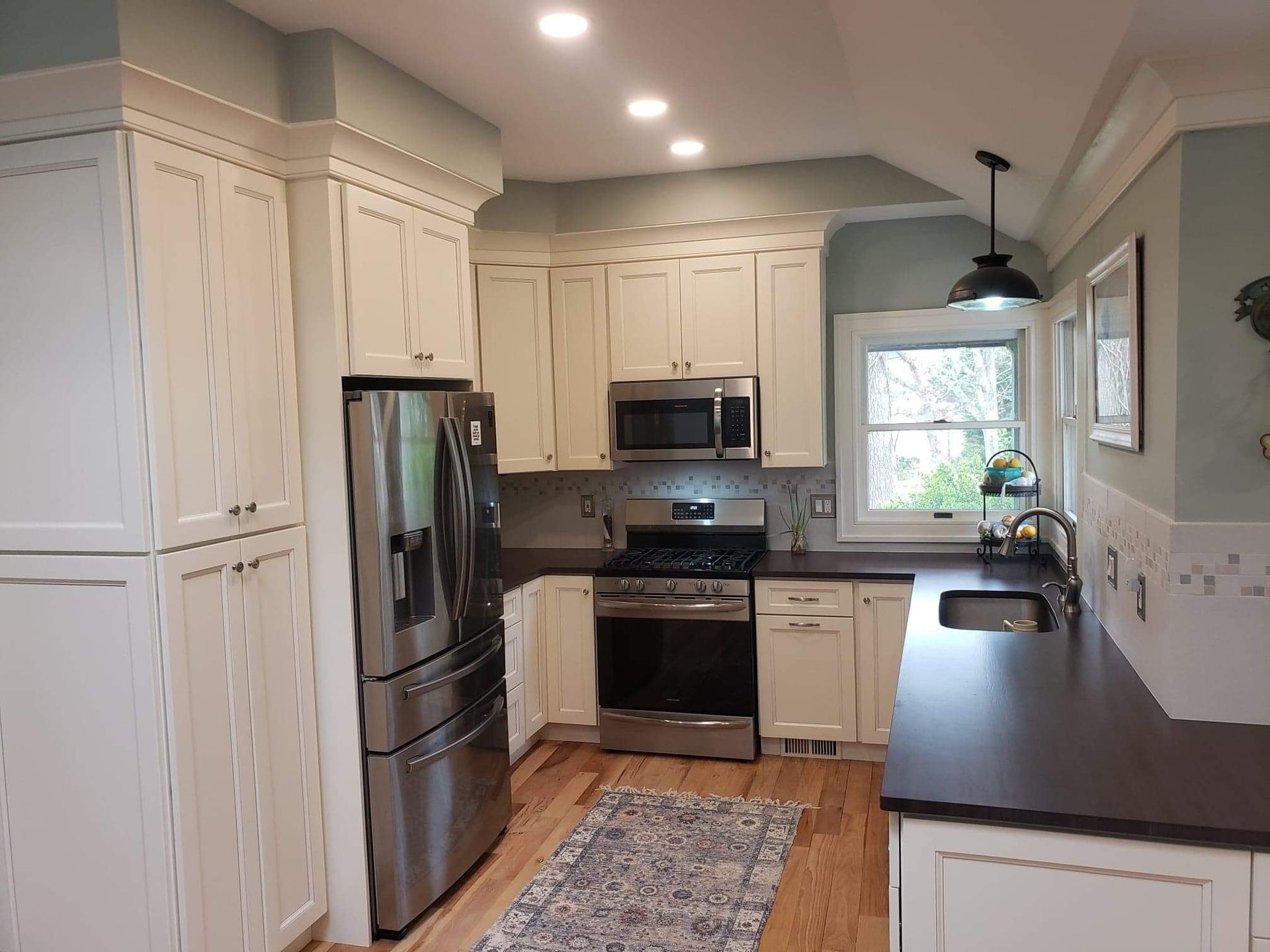A kitchen with white cabinets, windows, and stainless steel appliances