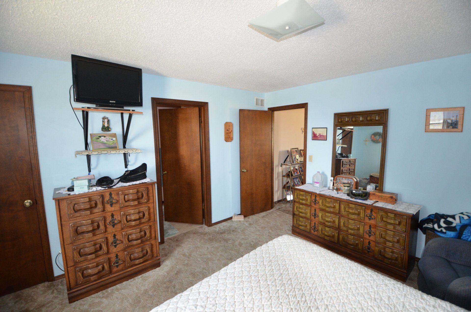 A bedroom with a bed , dresser , television and mirror.