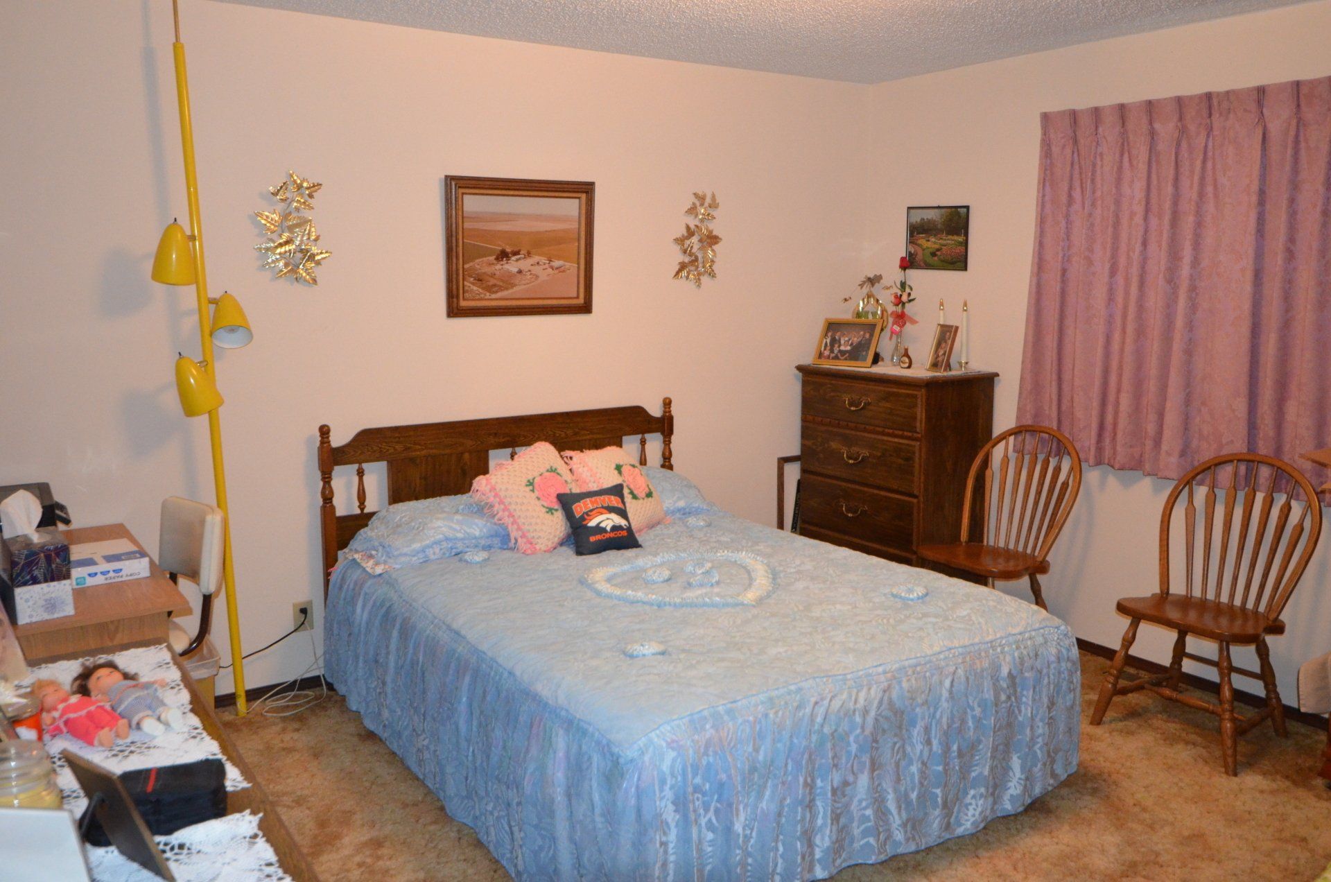 A bedroom with a bed , dresser , chairs and a picture on the wall.