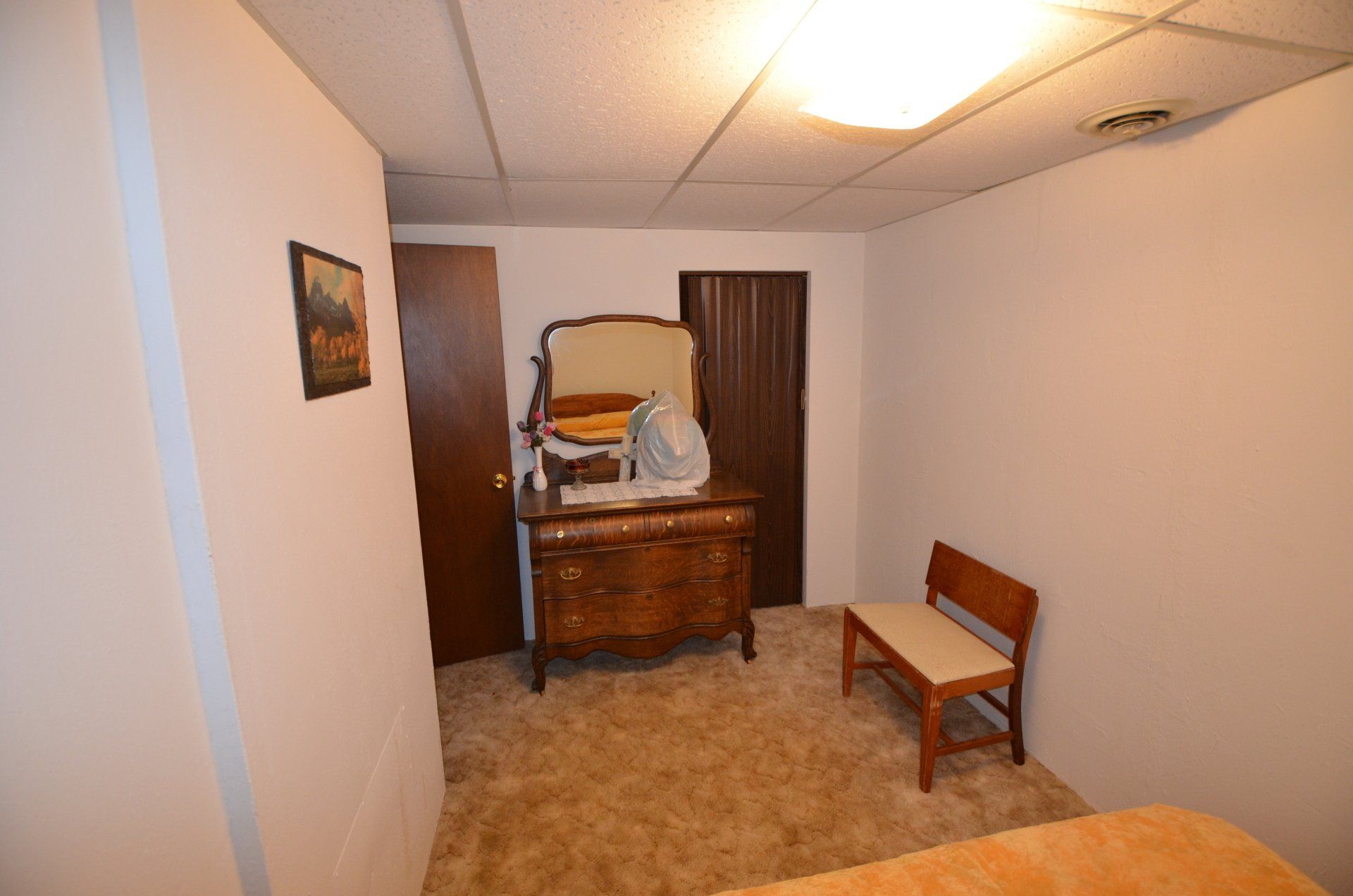A bedroom with a bed , dresser , mirror and bench.