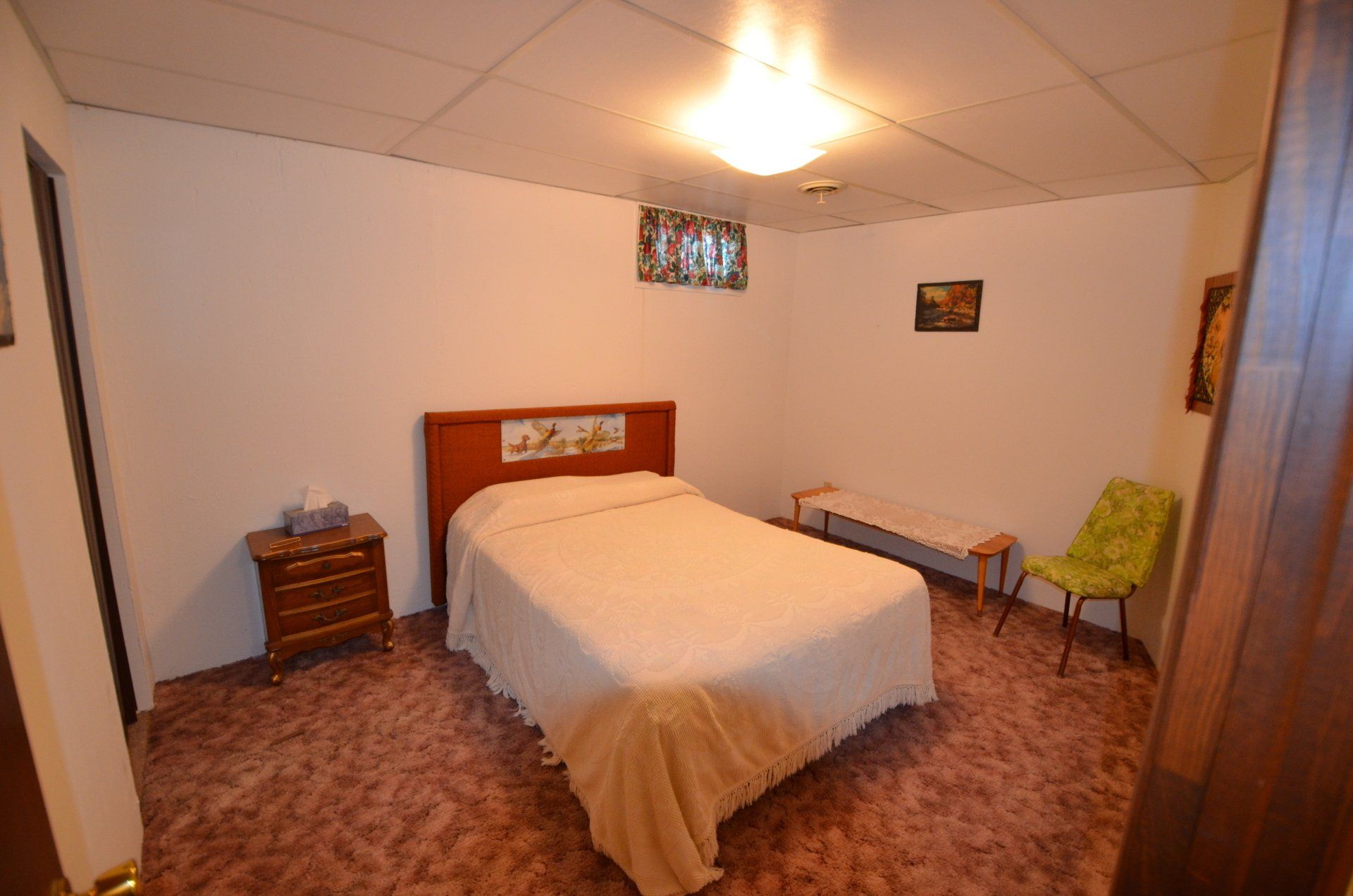 A bedroom with a bed , nightstand , chair and bench.