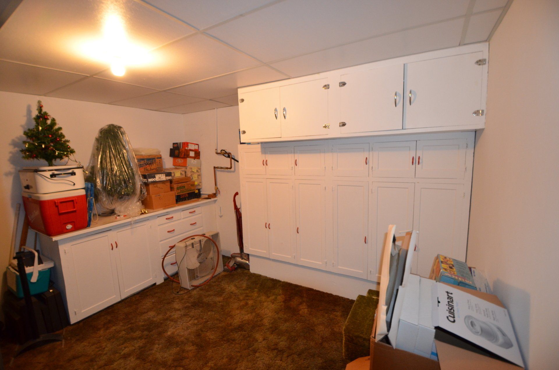 A room with white cabinets , boxes , a fan and a christmas tree.