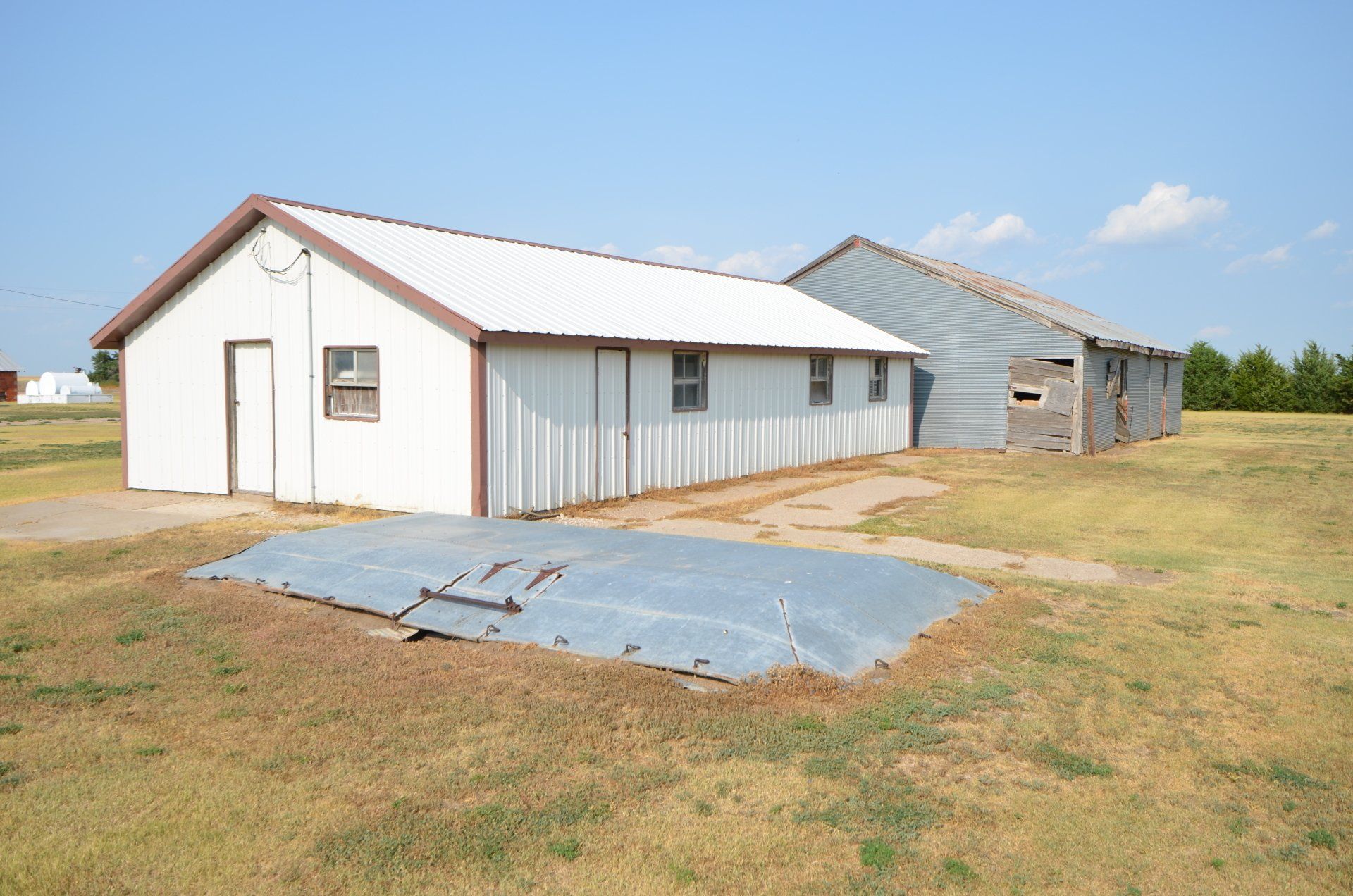 A white building with a brown roof is sitting in the middle of a grassy field.