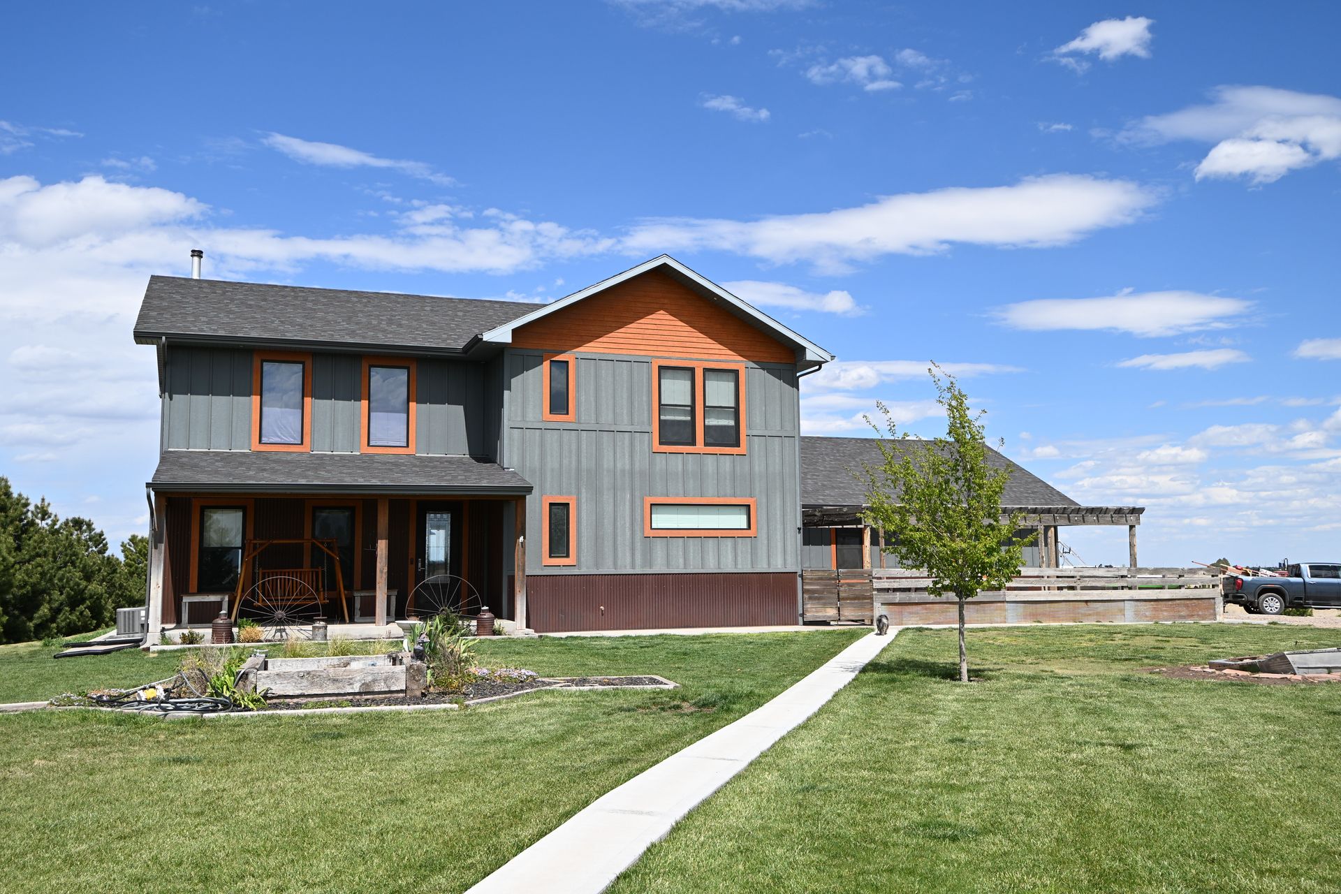 Modern two-story gray house with orange trim and a front porch under a blue sky