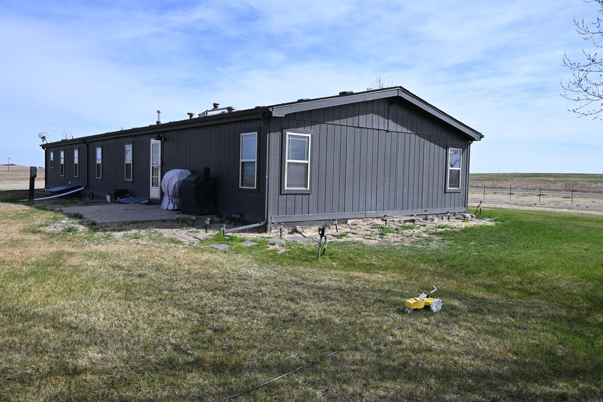 Gray farmhouse in a rural field under a clear sky, with a front porch and open landscape around it