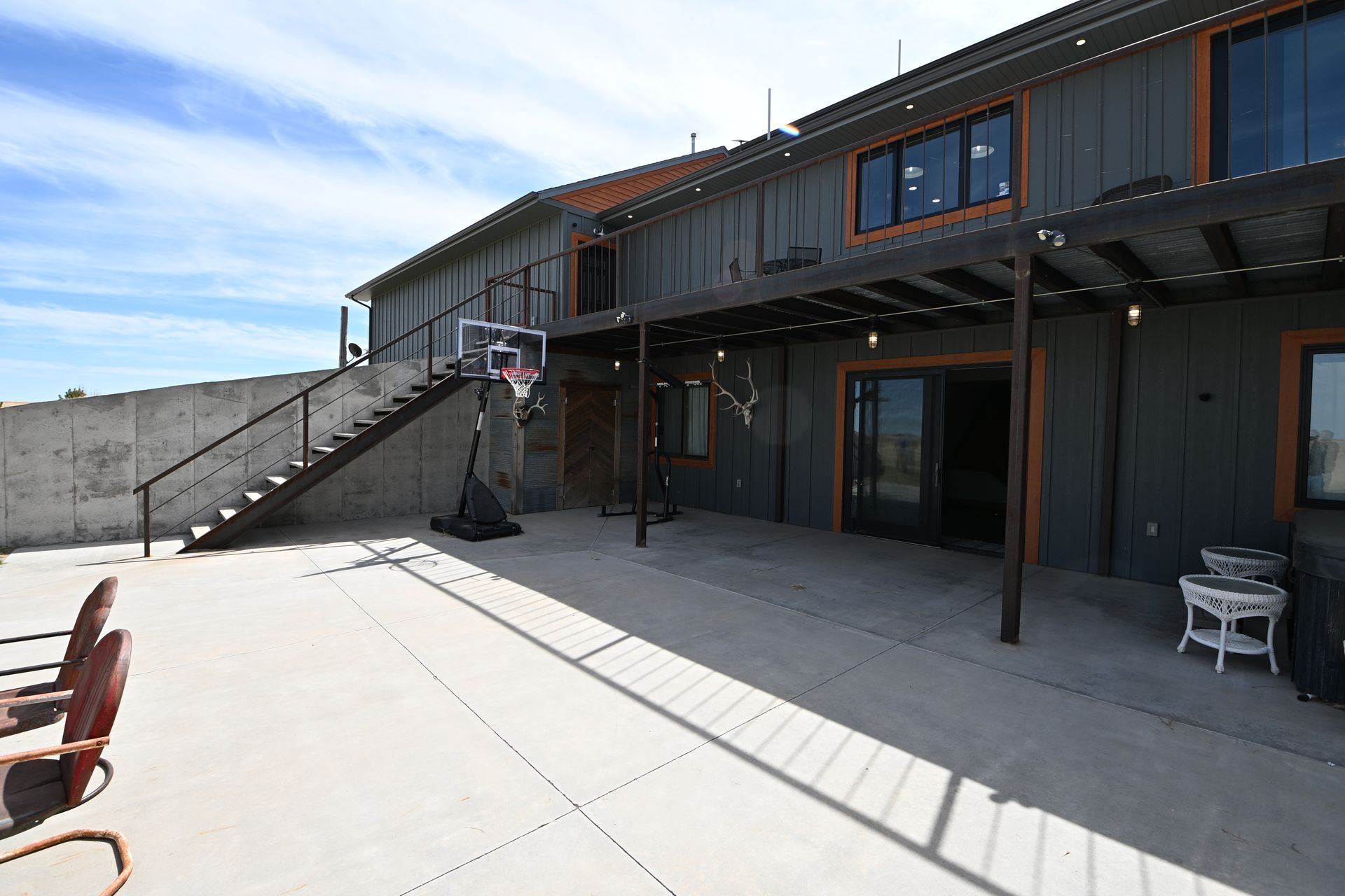 Exterior patio of a modern two-story building with stairs, patio chairs, and bright sunlight