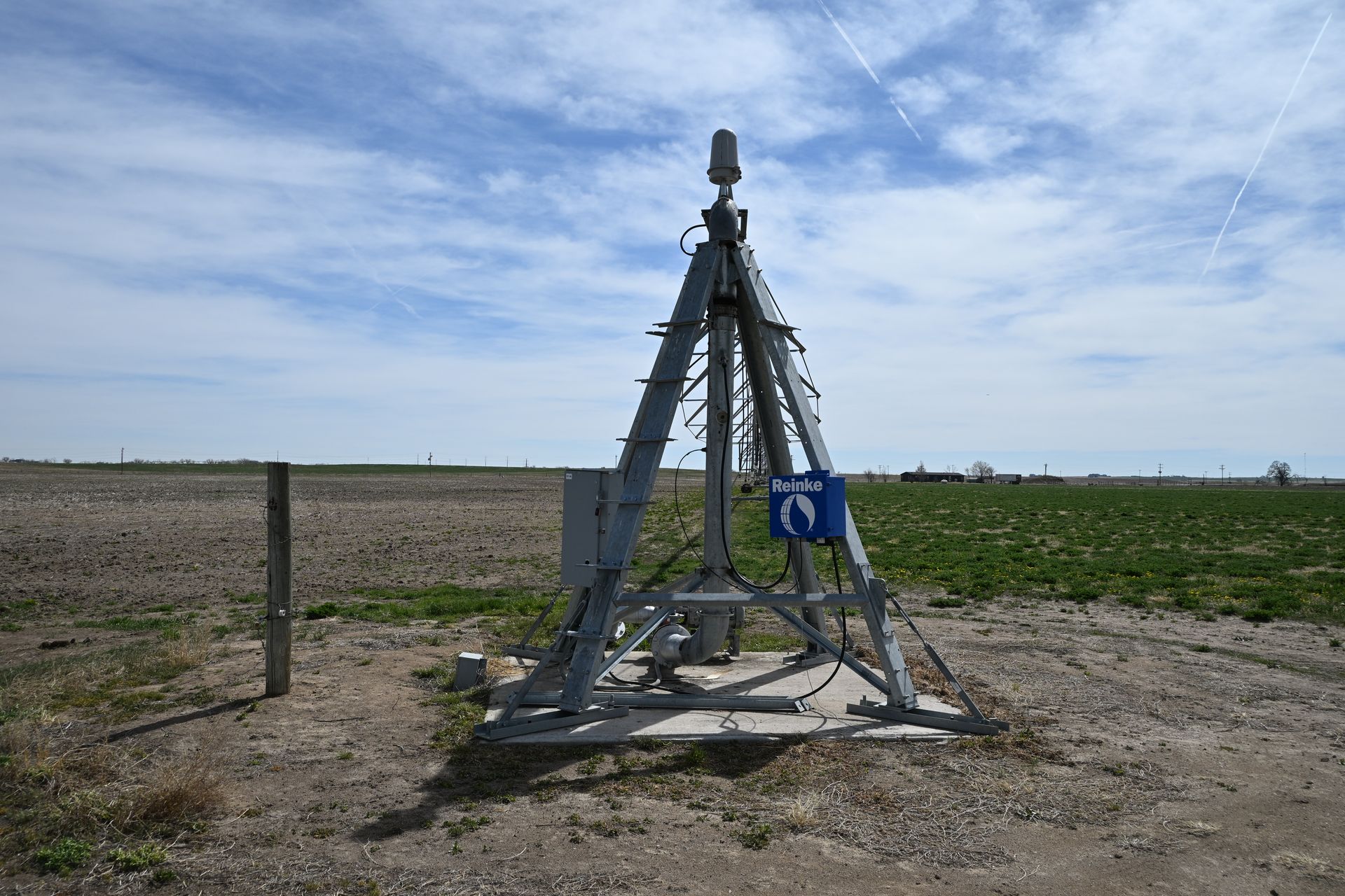 Metal weather instrument on a barren field under a partly cloudy sky
