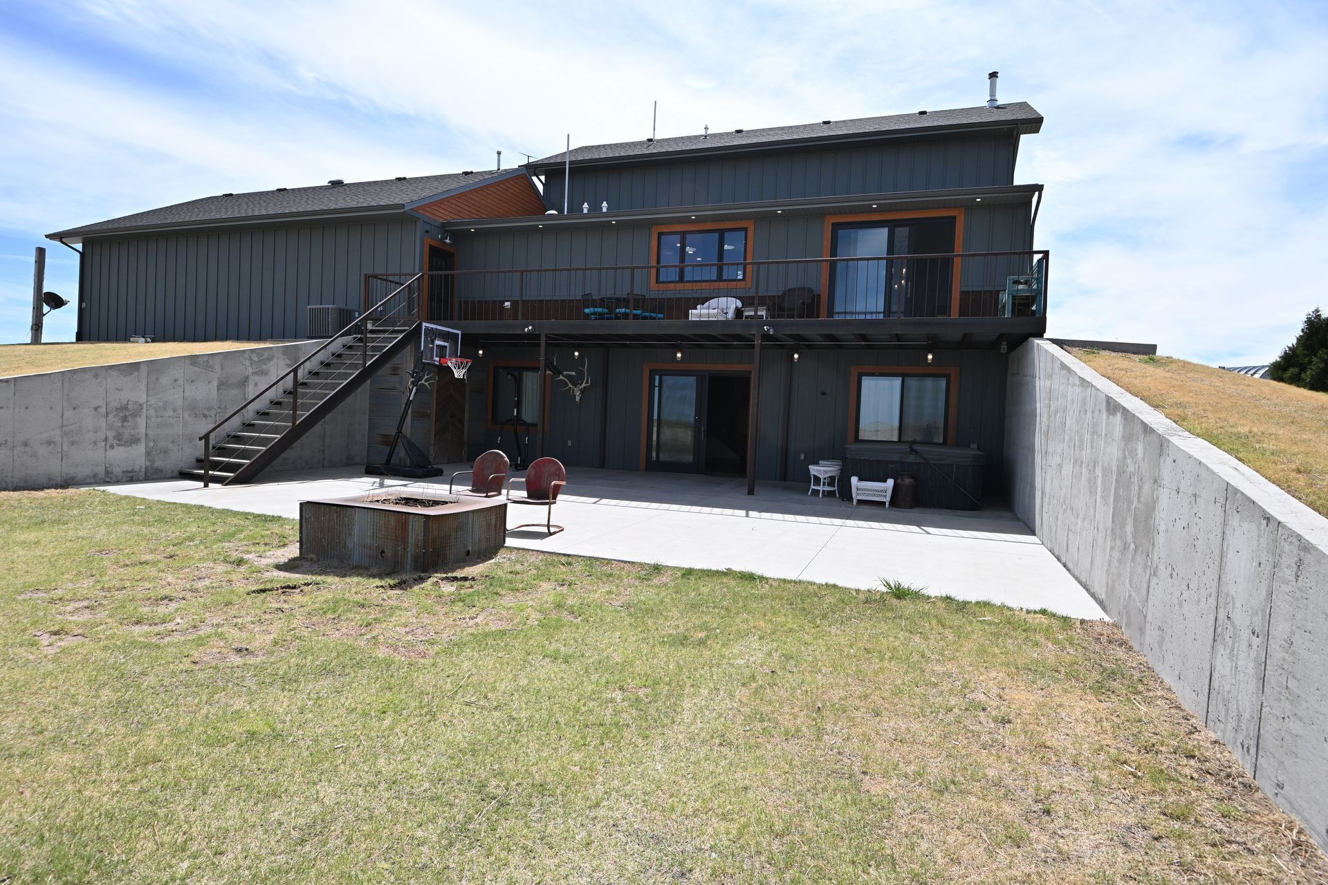Modern two-story house with a balcony, concrete walls, and a grassy yard under a clear sky
