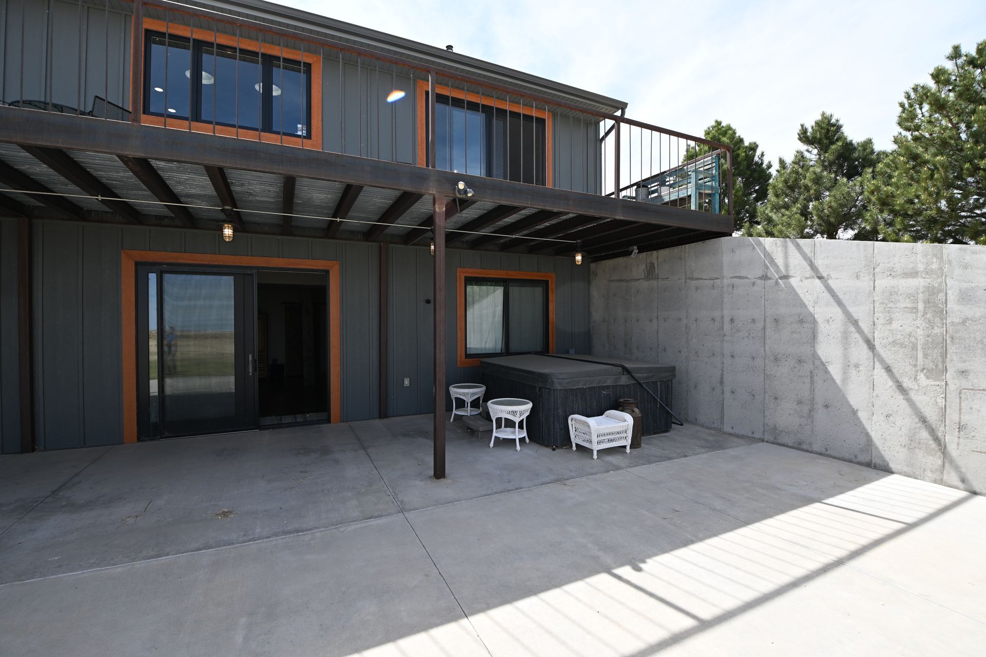 Modern two-story patio with gray walls, wood trim, pergola, and outdoor seating in a concrete courtyard