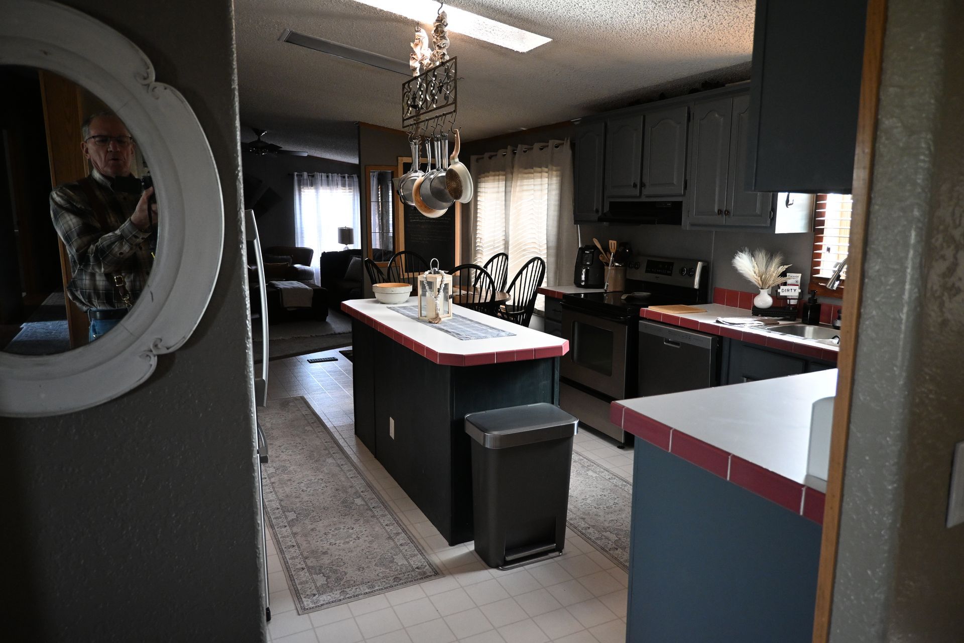 Modern kitchen with dark cabinets, red counters, an island, and a trash bin in the center.