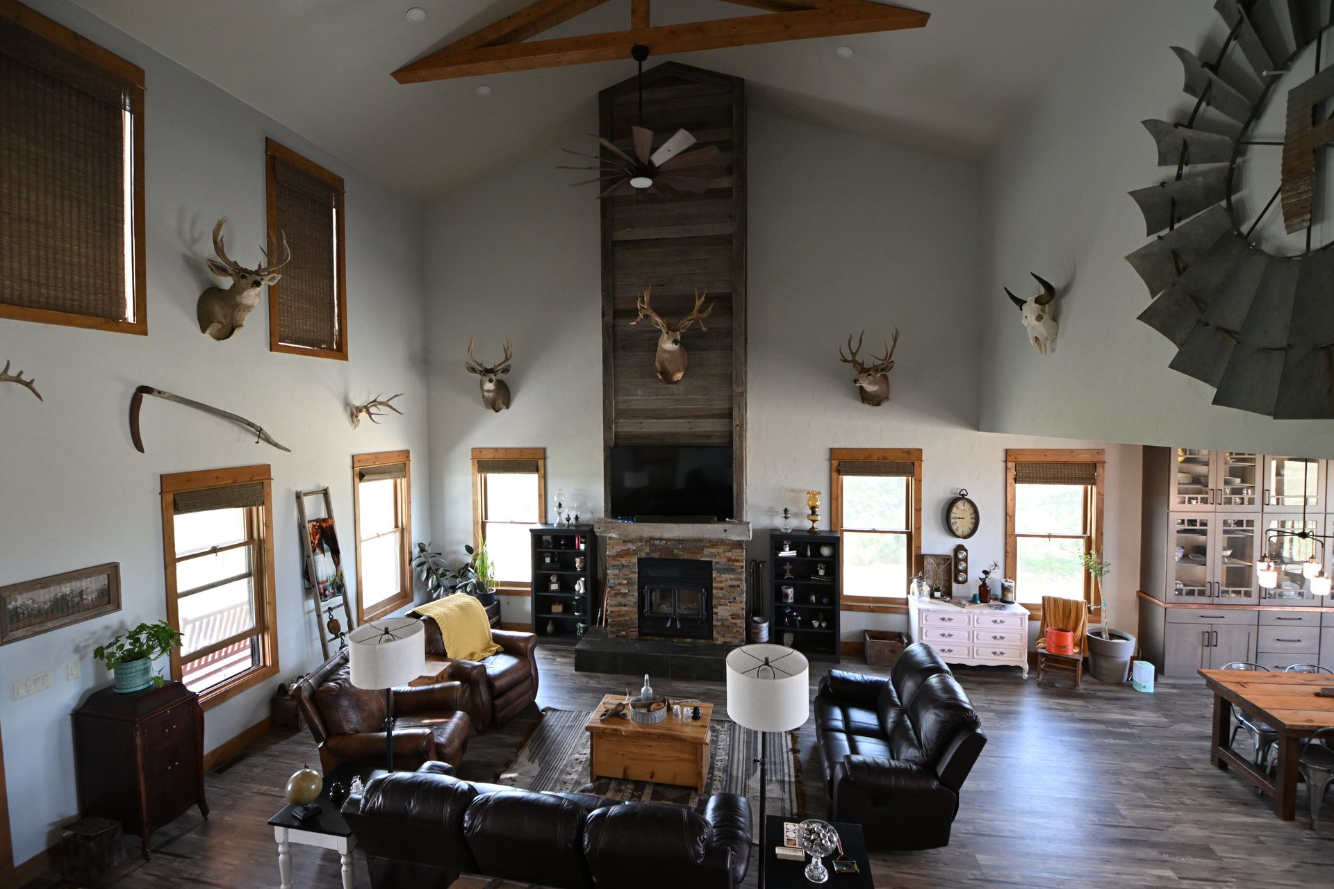 Rustic living room with leather chairs, stone fireplace, mounted antlers, and wood-beam ceiling