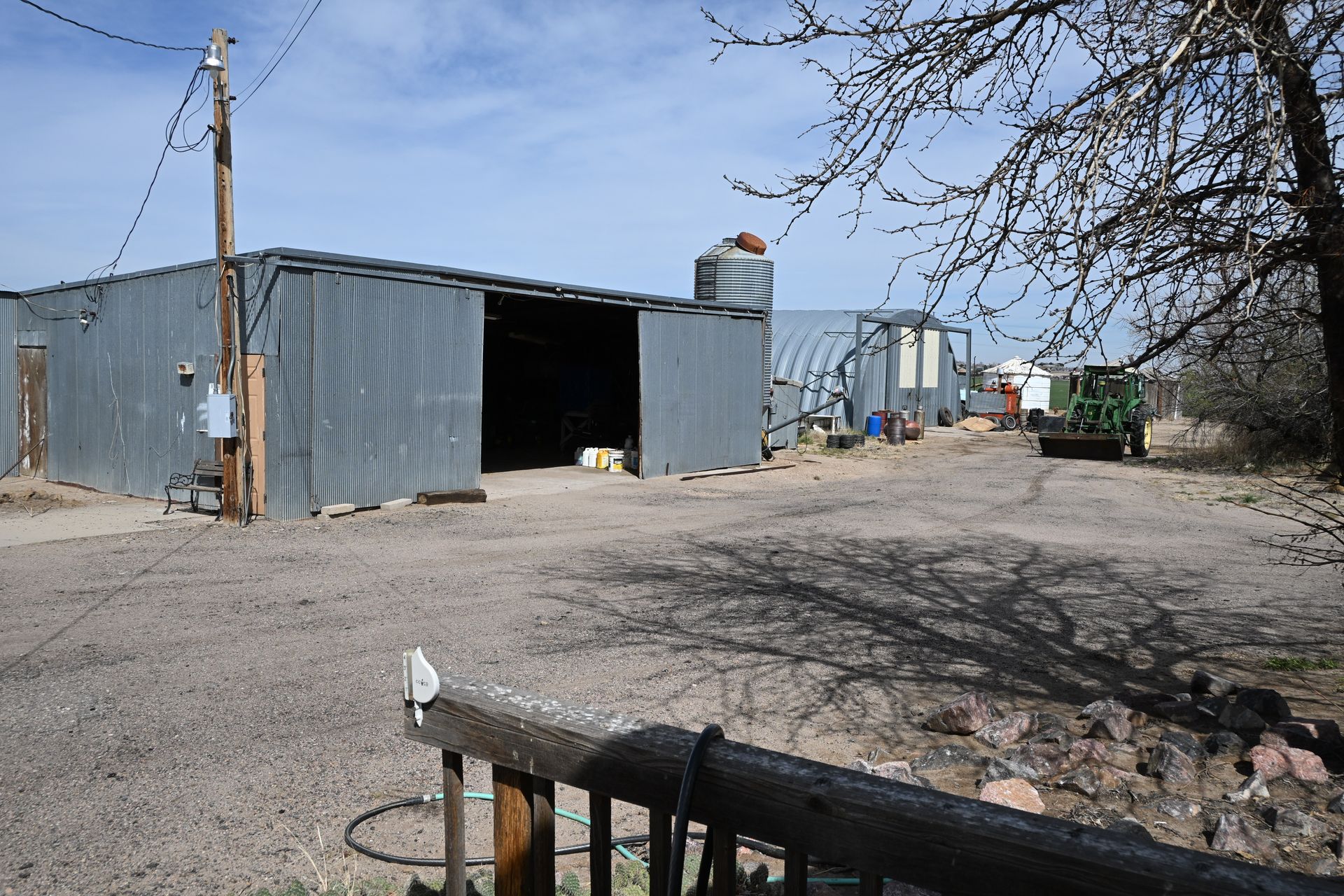 Rural yard with metal sheds, dirt ground, and a utility pole under a clear sky