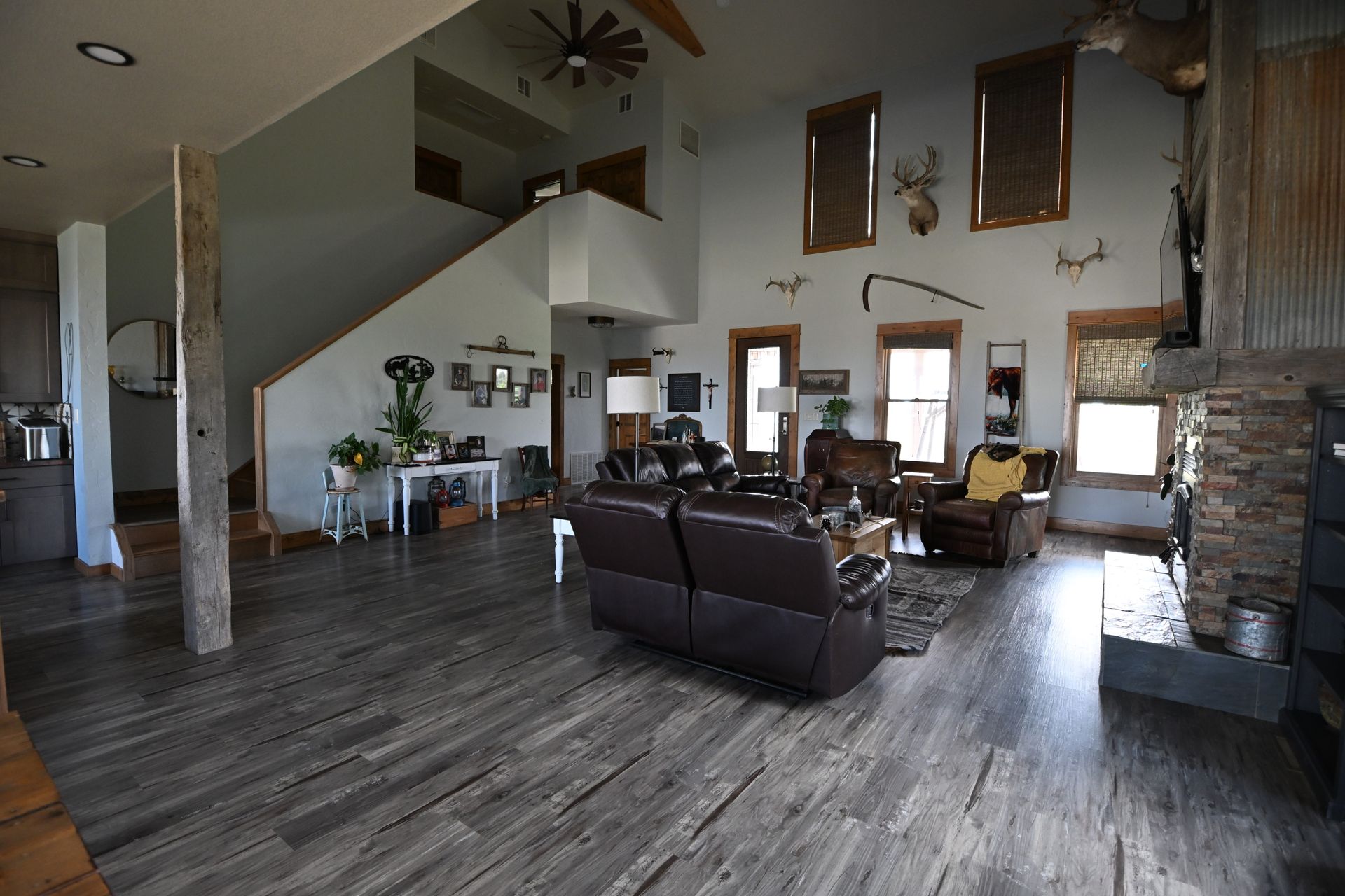 Spacious modern living room with dark wood floors, leather sofas, staircase, and stone fireplace