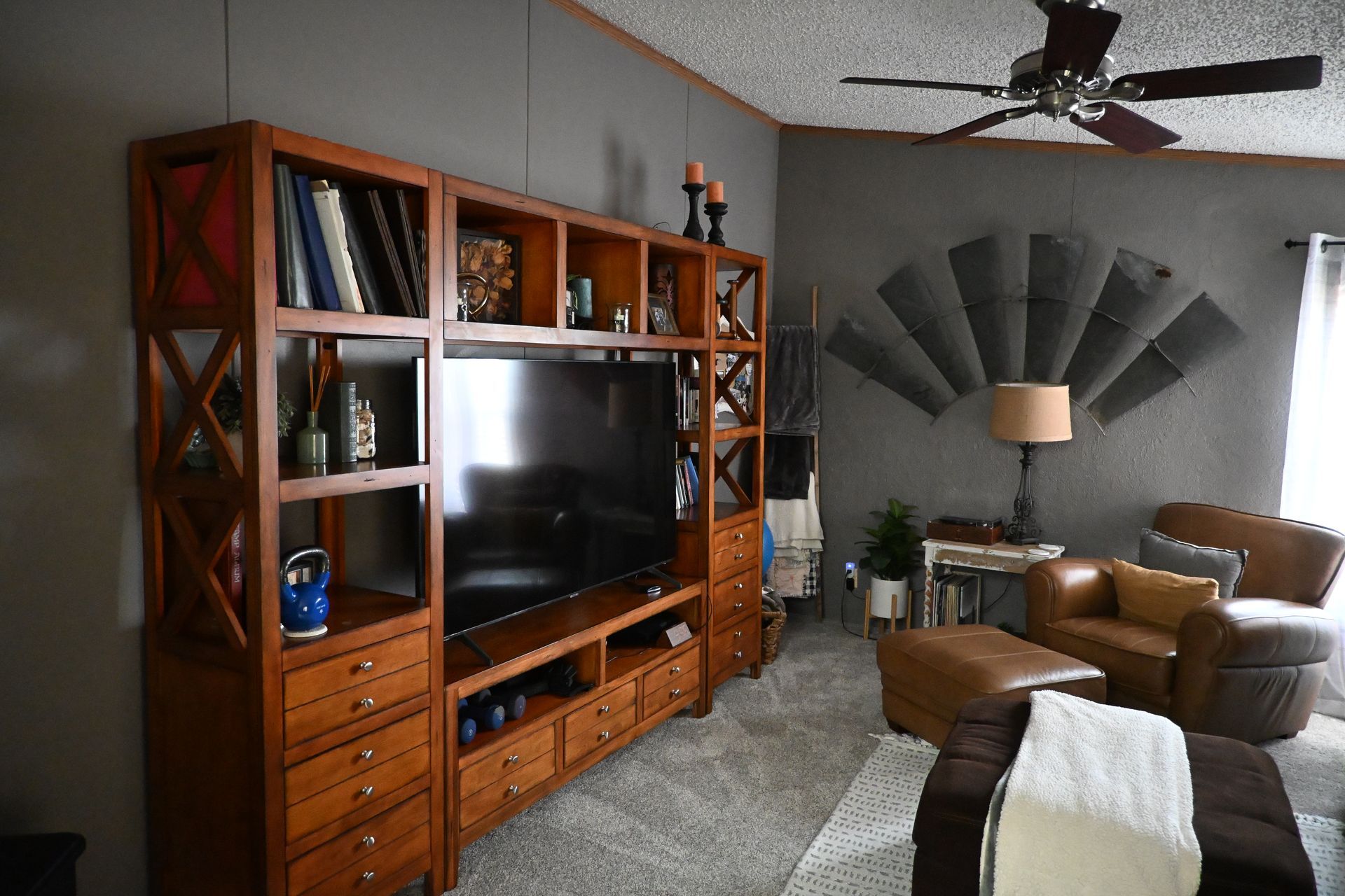 Living room with a wooden entertainment center, TV, fan, sofa, and floor lamp.