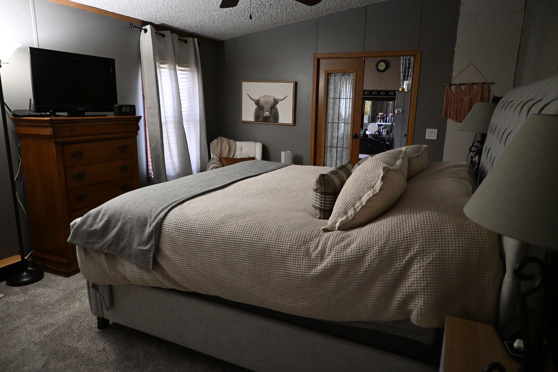 Cozy bedroom with a made bed, dresser, TV, lamp, and wall art under a tray ceiling