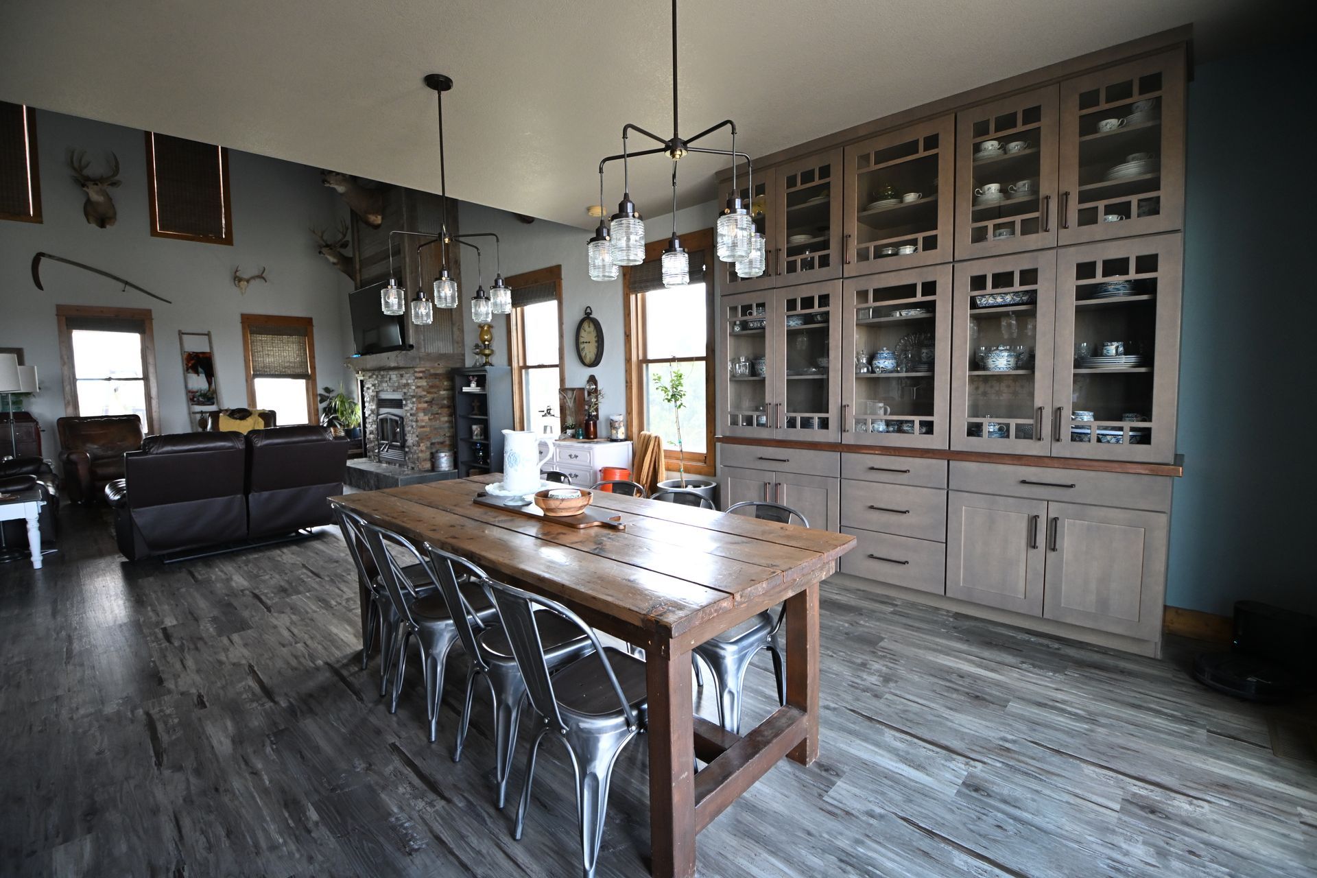 Modern dining room with a long wooden table, metal chairs, and glass-front cabinets along the wall