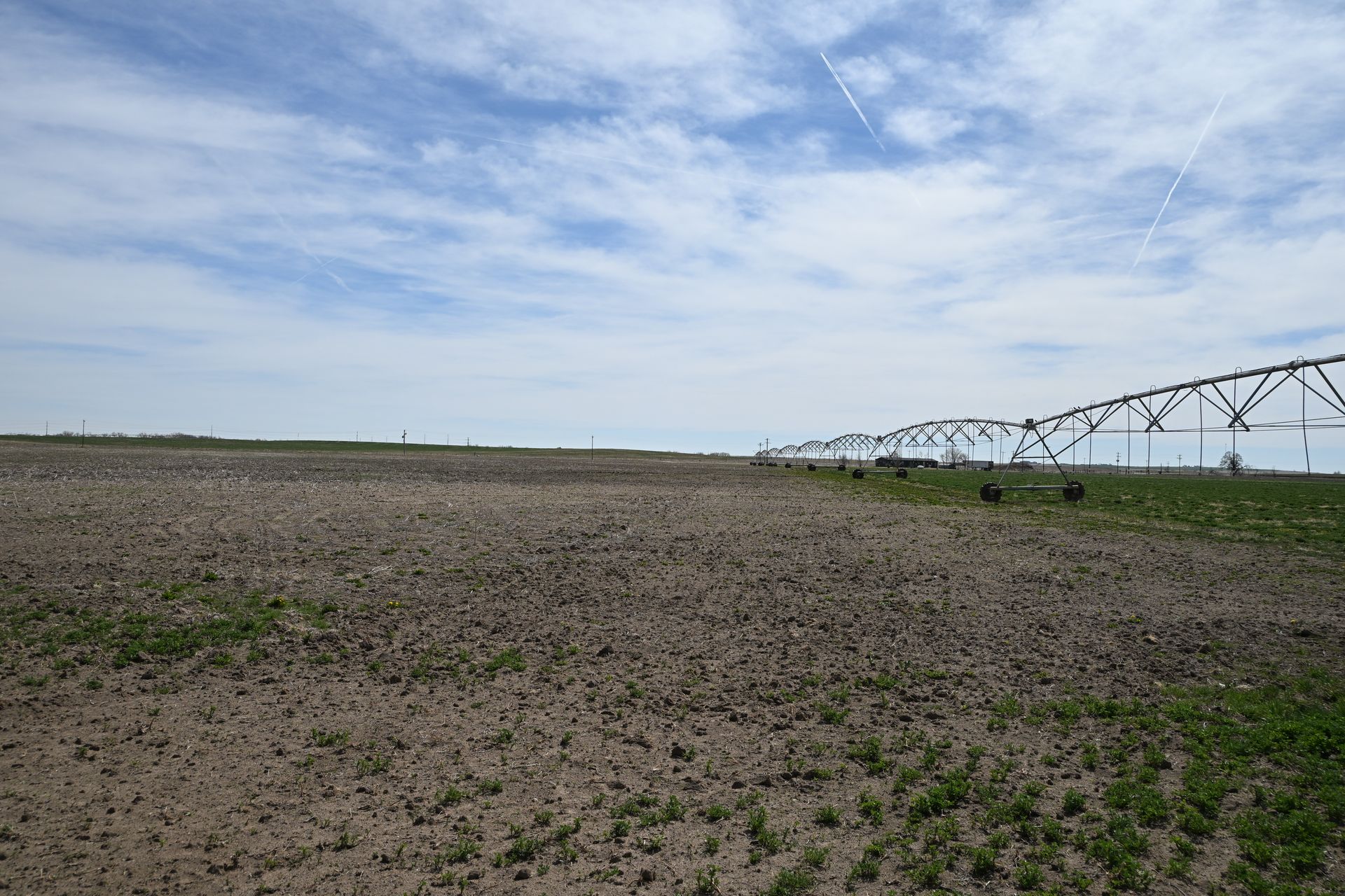 A wide plowed field under a cloudy sky with a center-pivot irrigation system on the right.