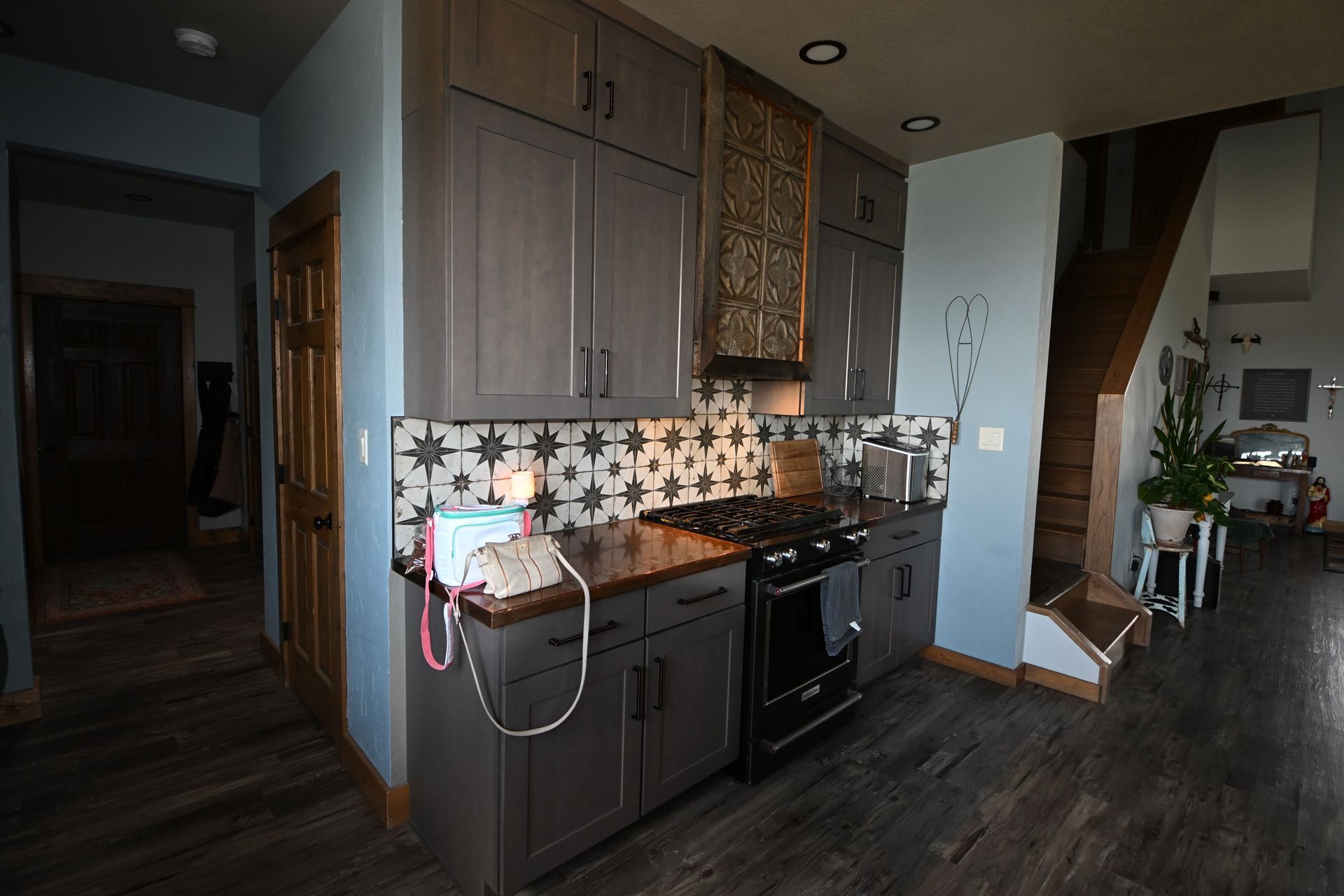 Compact kitchen with dark cabinets, black stove, patterned backsplash, and a hallway opening to the left