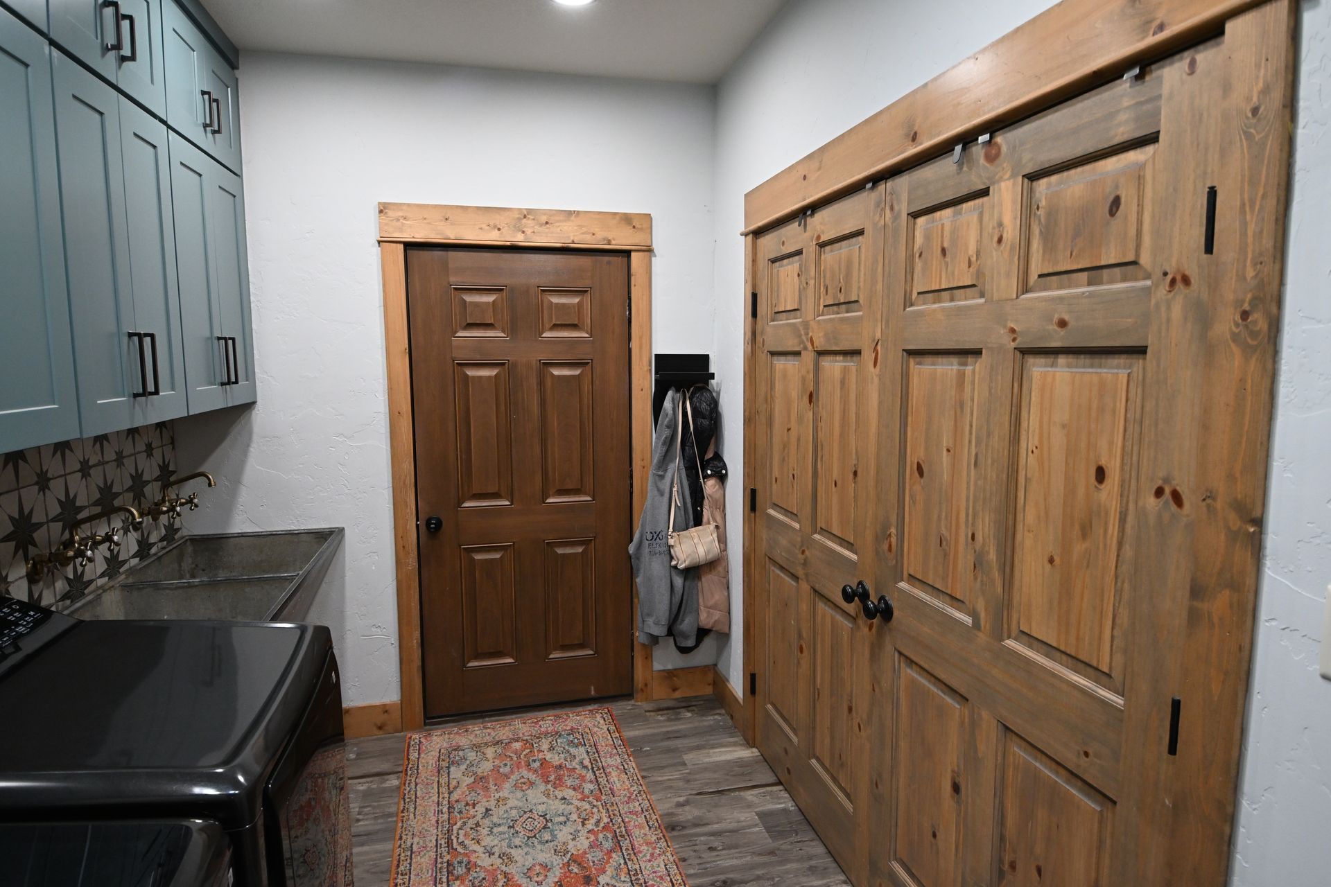 Narrow kitchen with blue cabinets, black countertop, wood doors, and a patterned rug.