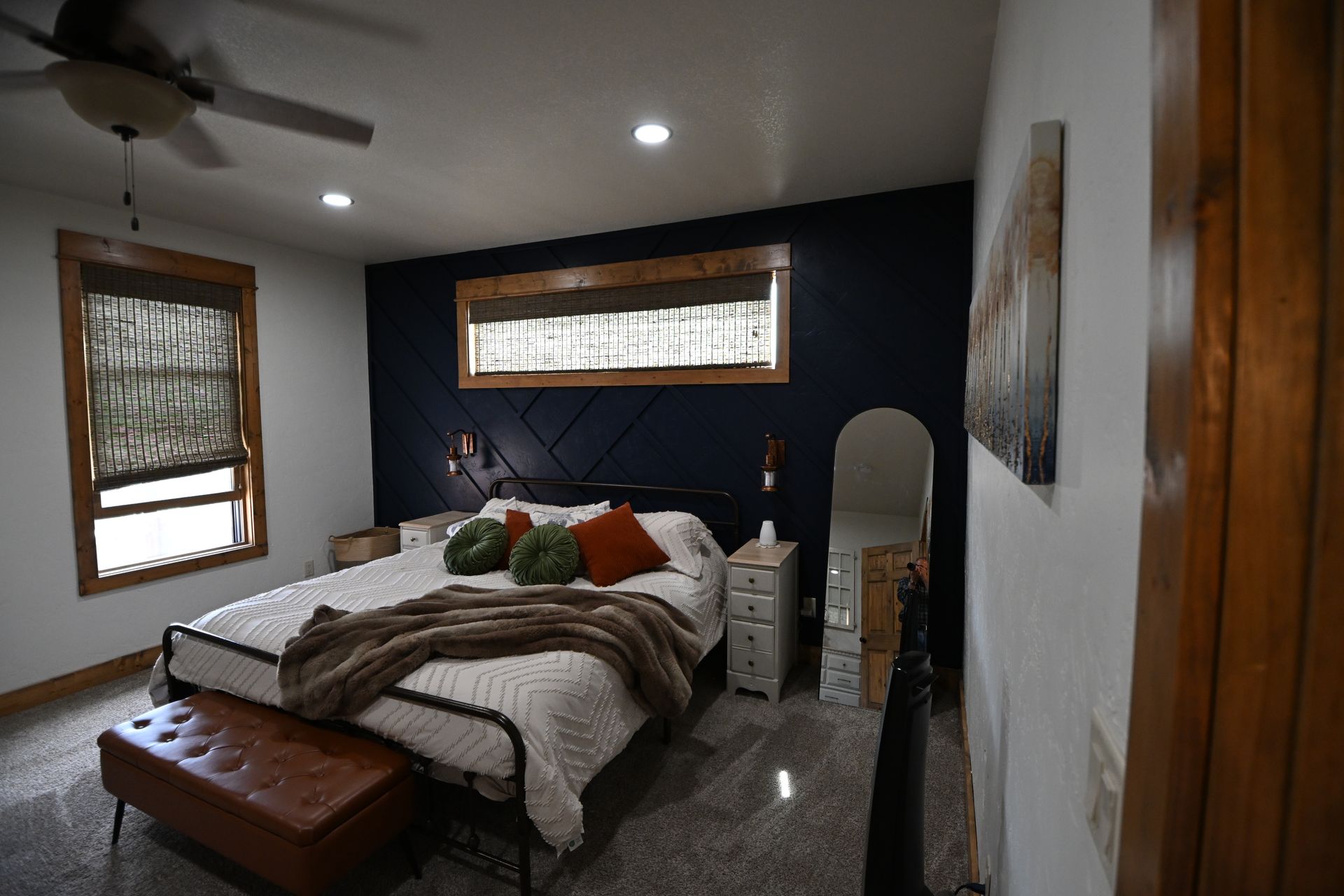 Cozy bedroom with a bed, brown bench, dark accent wall, and small windows letting in soft light