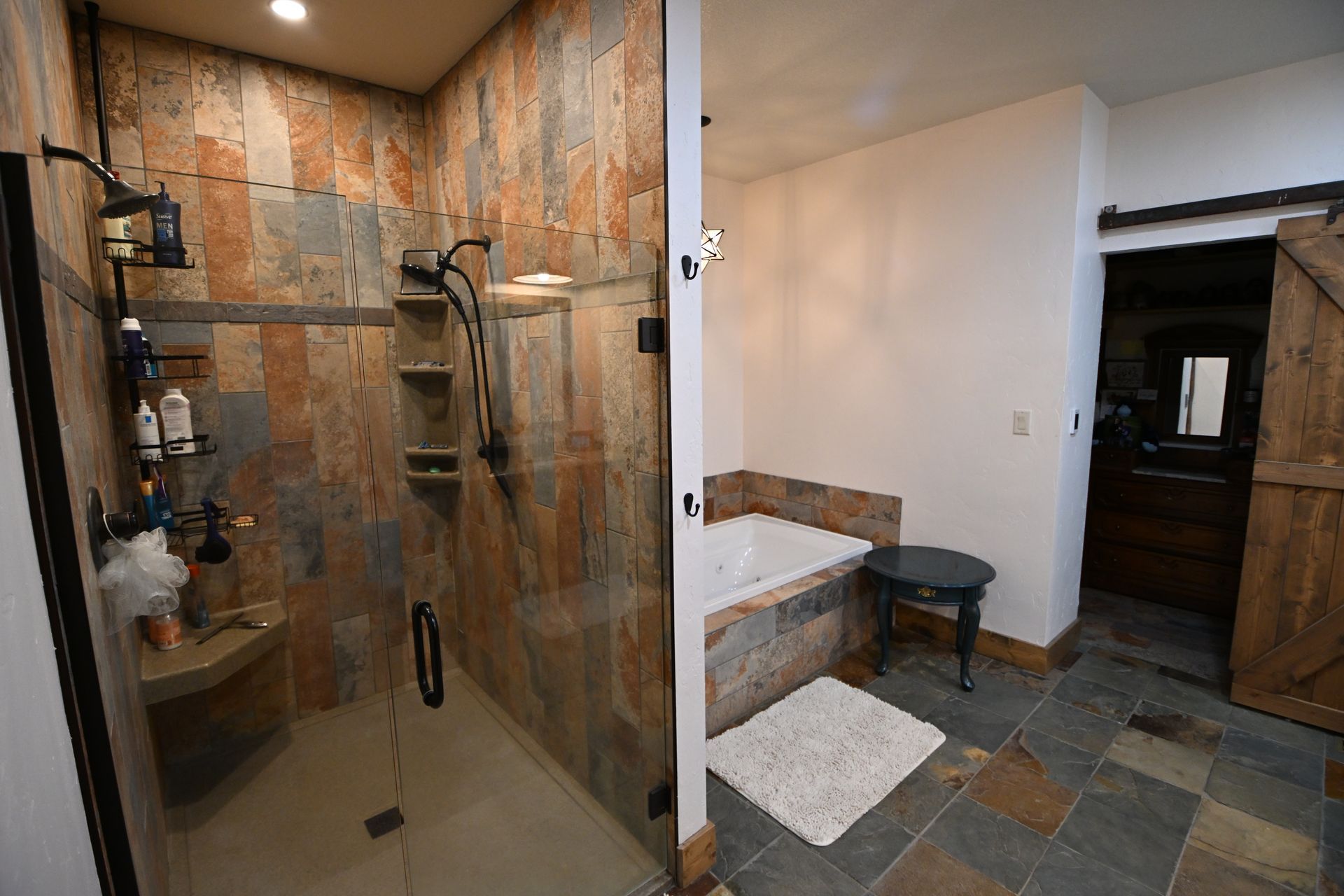Bathroom with tiled walk-in shower, glass door, and a small stool beside a raised step.