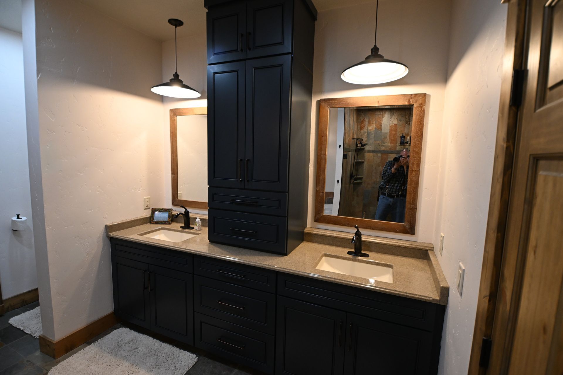 Modern bathroom vanity with dark cabinets, beige countertop, two mirrors, and pendant lights