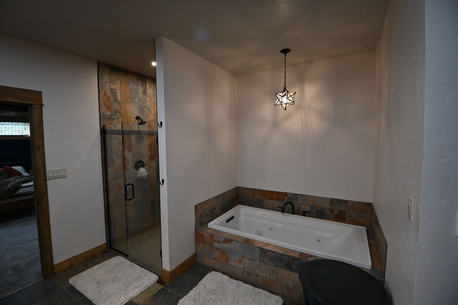 Modern bathroom with walk-in shower, soaking tub, and pendant light on tiled walls