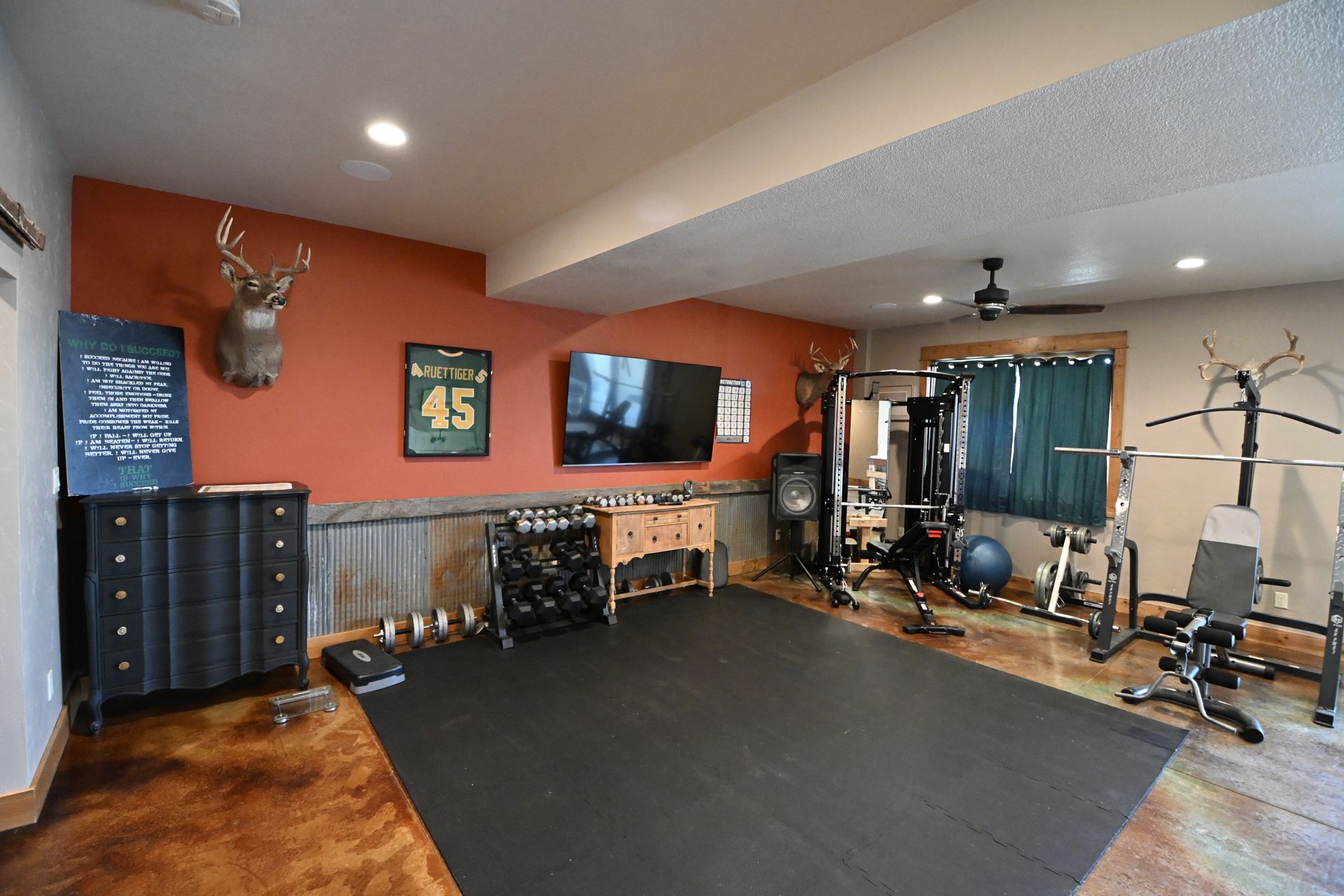 Home gym with black mats, weight machines, TV, and orange walls