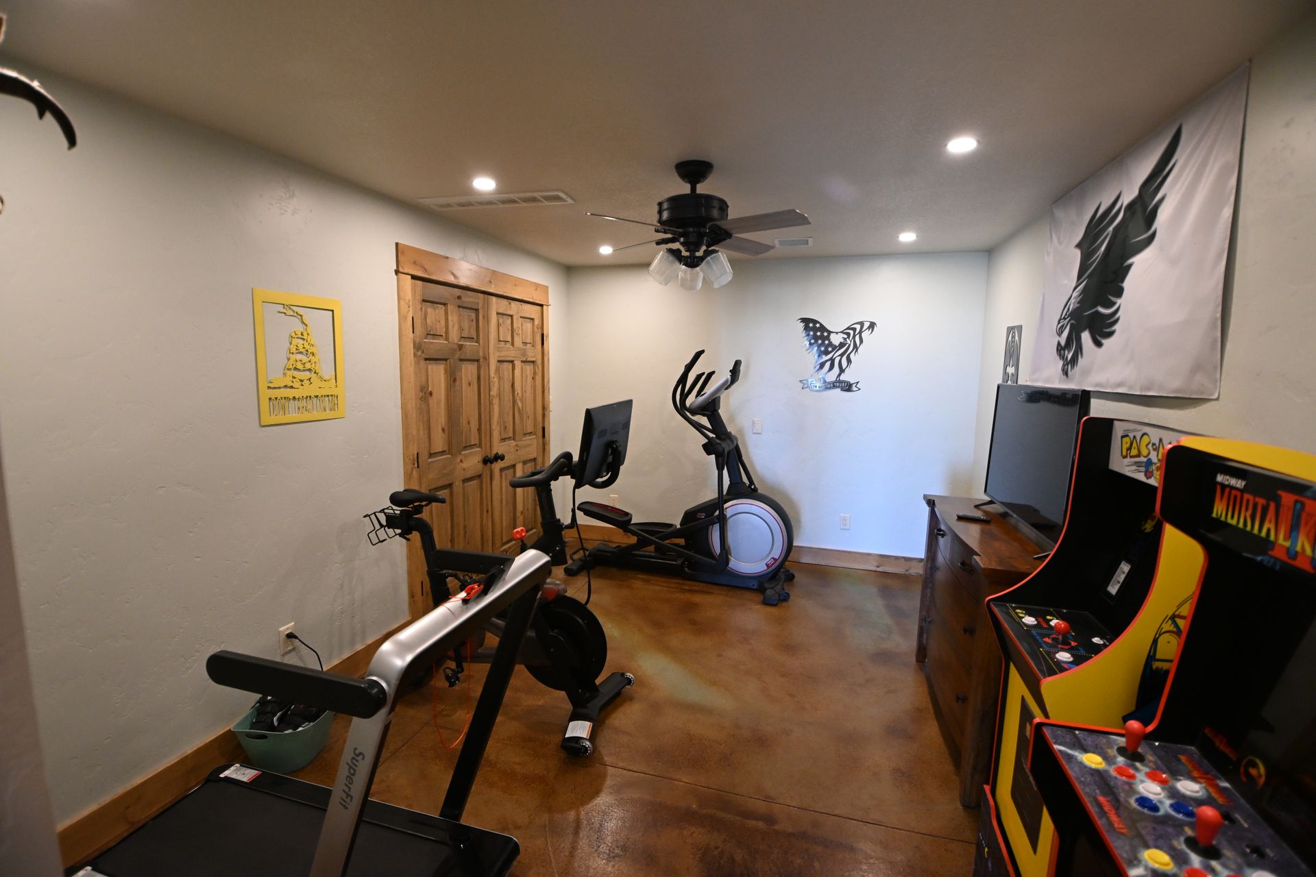 Home workout room with exercise bike, bench, fan, wall decor, and arcade cabinet