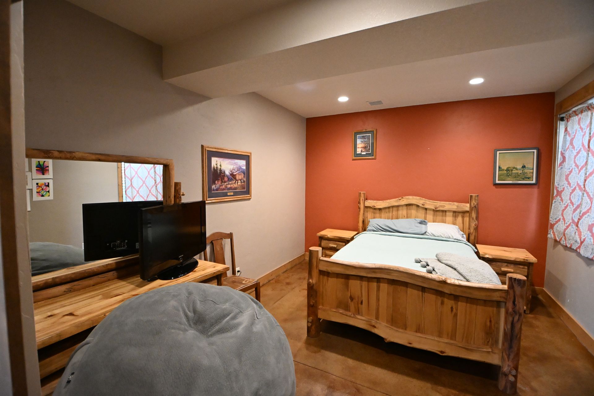 Cozy bedroom with wooden bed, orange accent wall, TV, and rustic decor