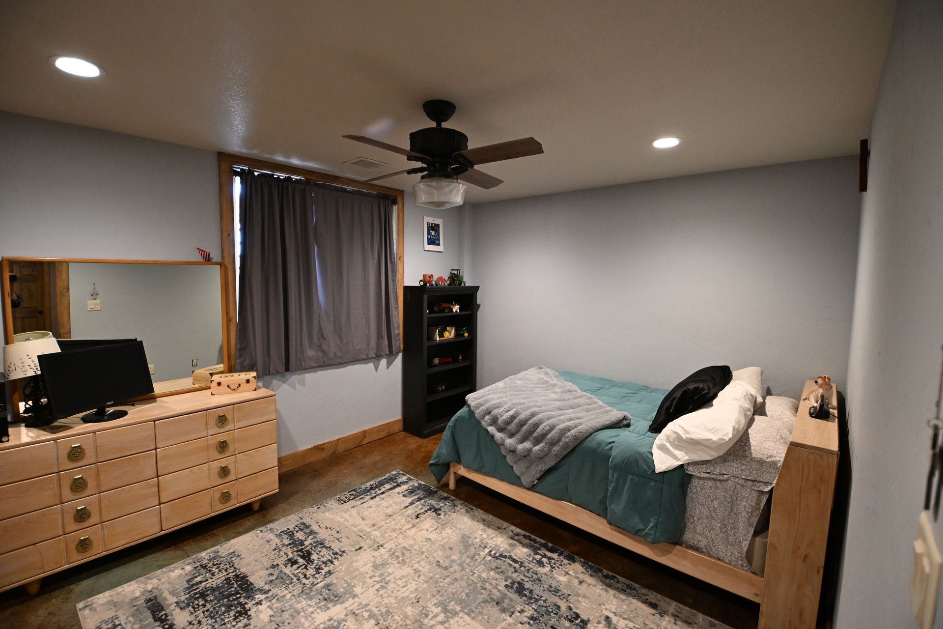 Modern bedroom with bed, dresser, desk, window, and ceiling fan on gray walls