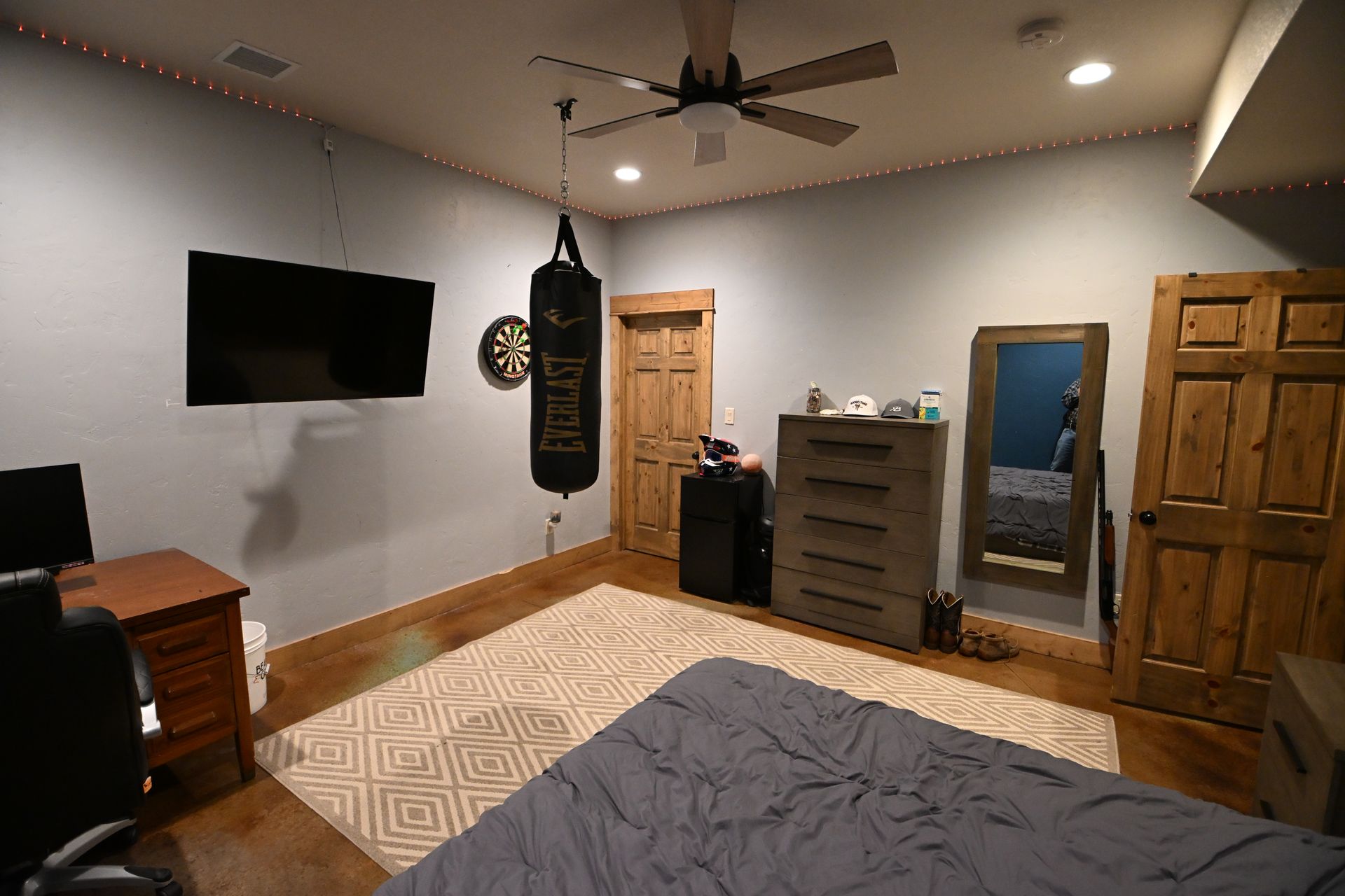 Bedroom with a bed, wall-mounted TV, punching bag, dresser, and ceiling fan in a warm-toned room
