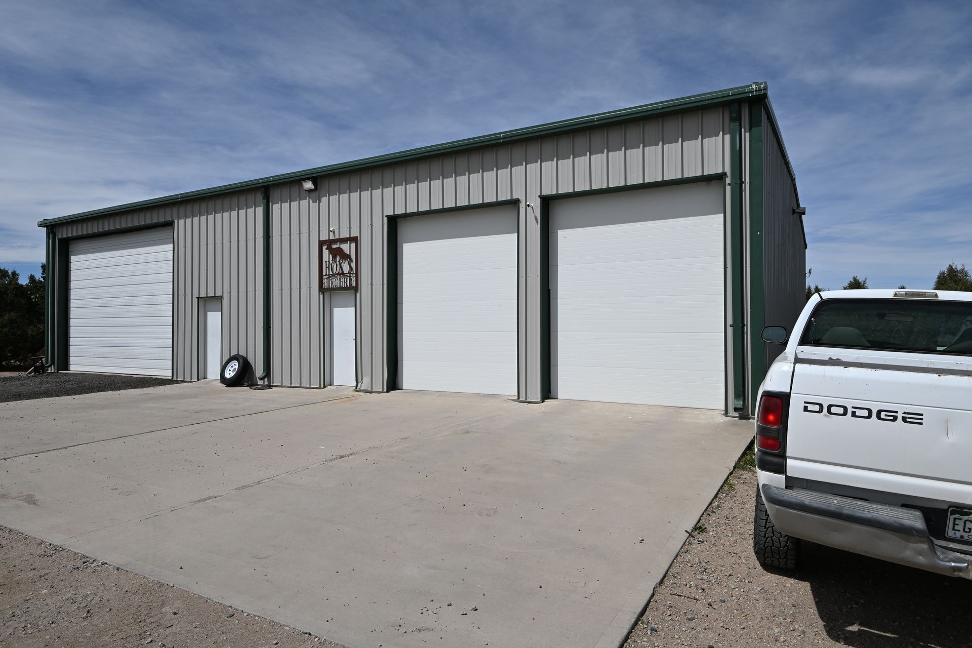 Gray metal industrial building with two white garage doors and a white pickup truck in front