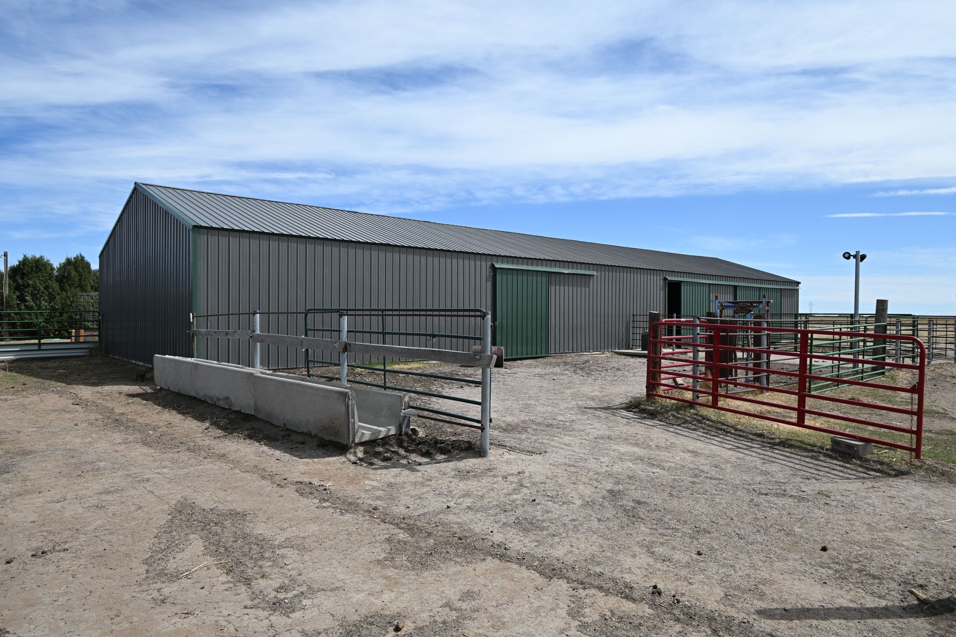 Rural metal barn with fenced livestock pens and a gravel yard under a blue sky