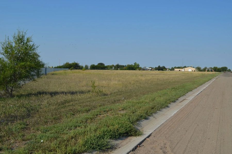 Empty, grassy lot next to a paved road under a clear blue sky.