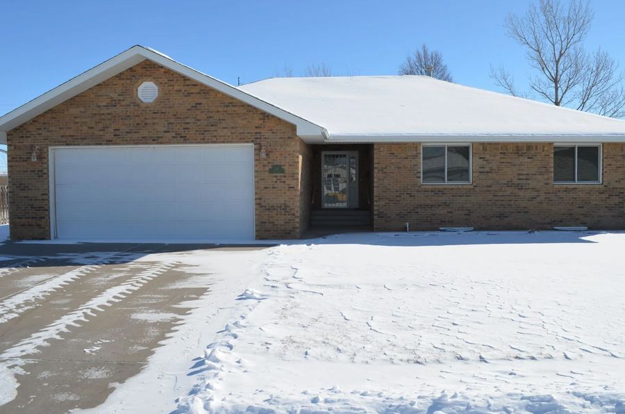 Brick house covered in snow, garage, driveway, and winter landscape.