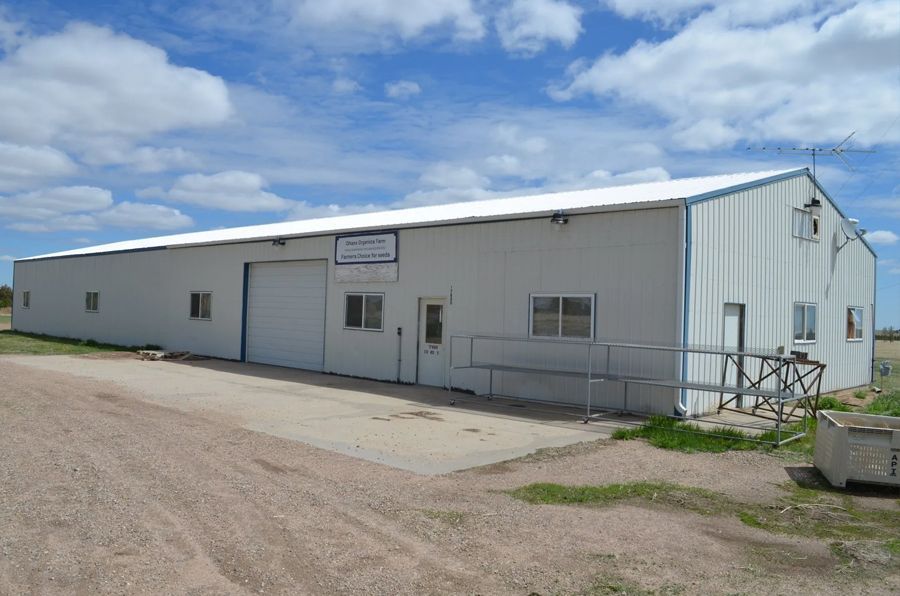 White industrial building with a blue trim, small windows, and a ramp leading to the door on a sunny day.