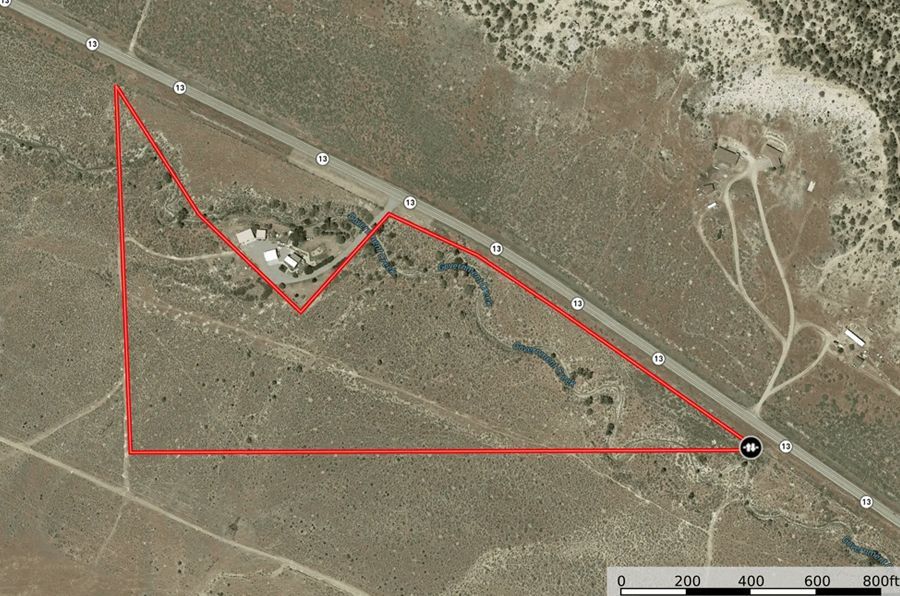 Aerial view of a plot of land outlined in red along a highway, with buildings and sparse vegetation.
