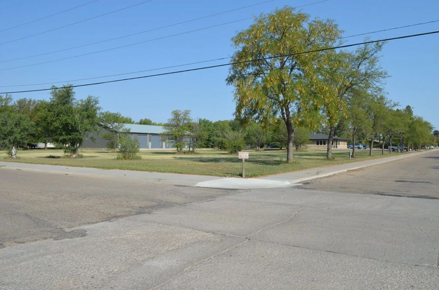 Street corner with trees and a building in the background on a sunny day.