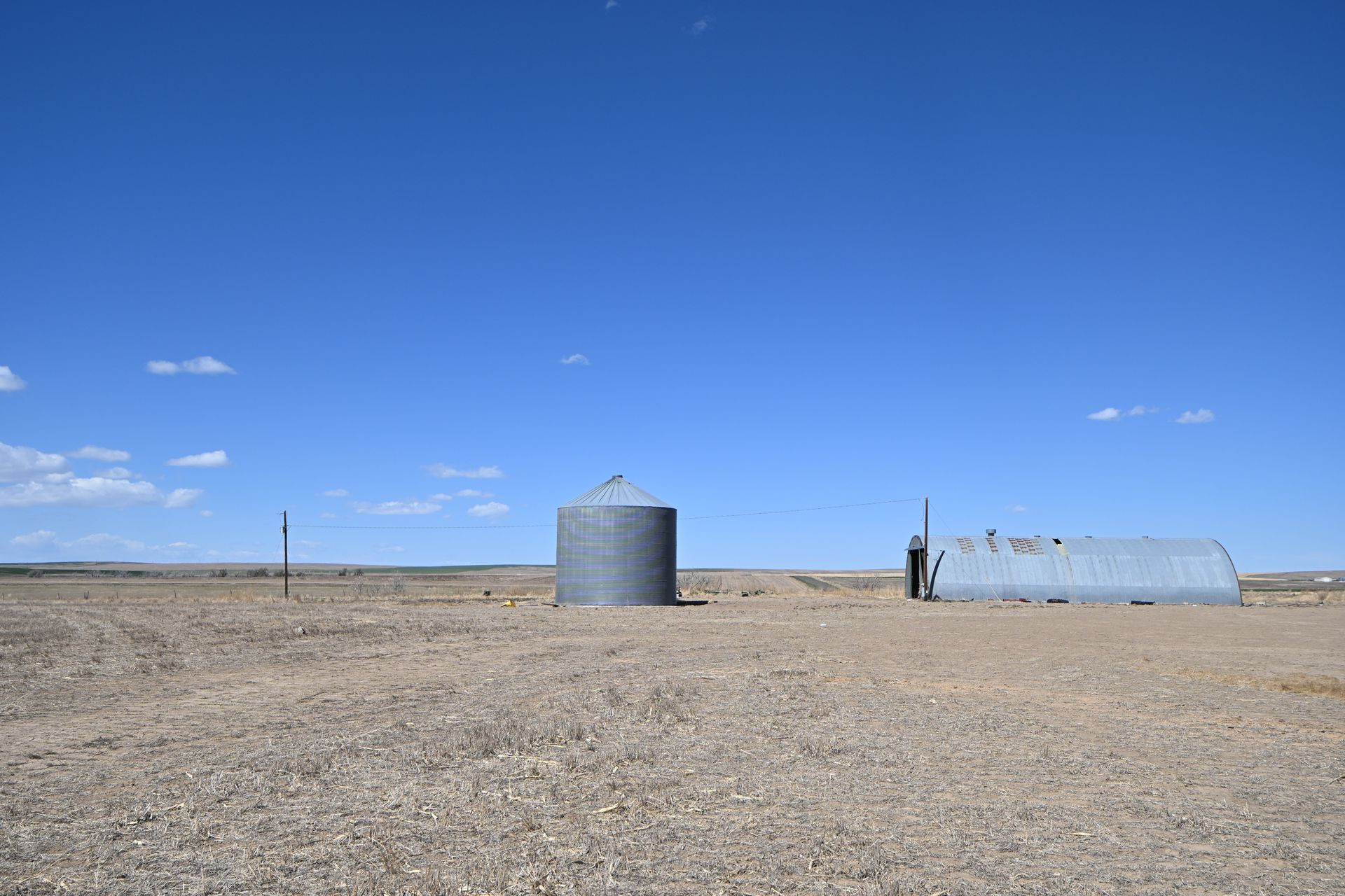 Desert landscape with a silver silo, small structure, and blue sky over flat gravel ground