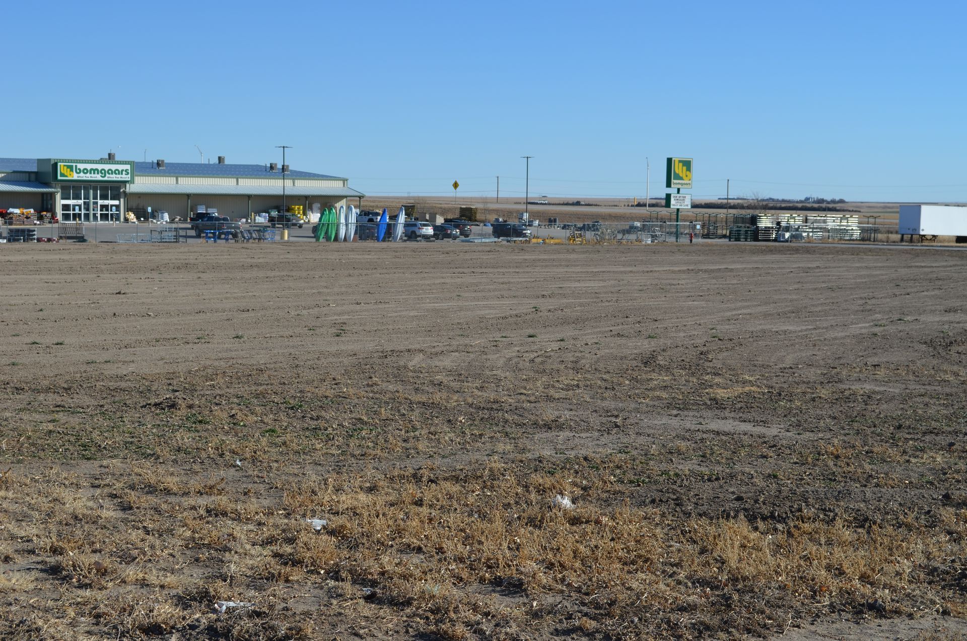 A hardware store with outdoor displays, viewed from a dirt field on a sunny day.
