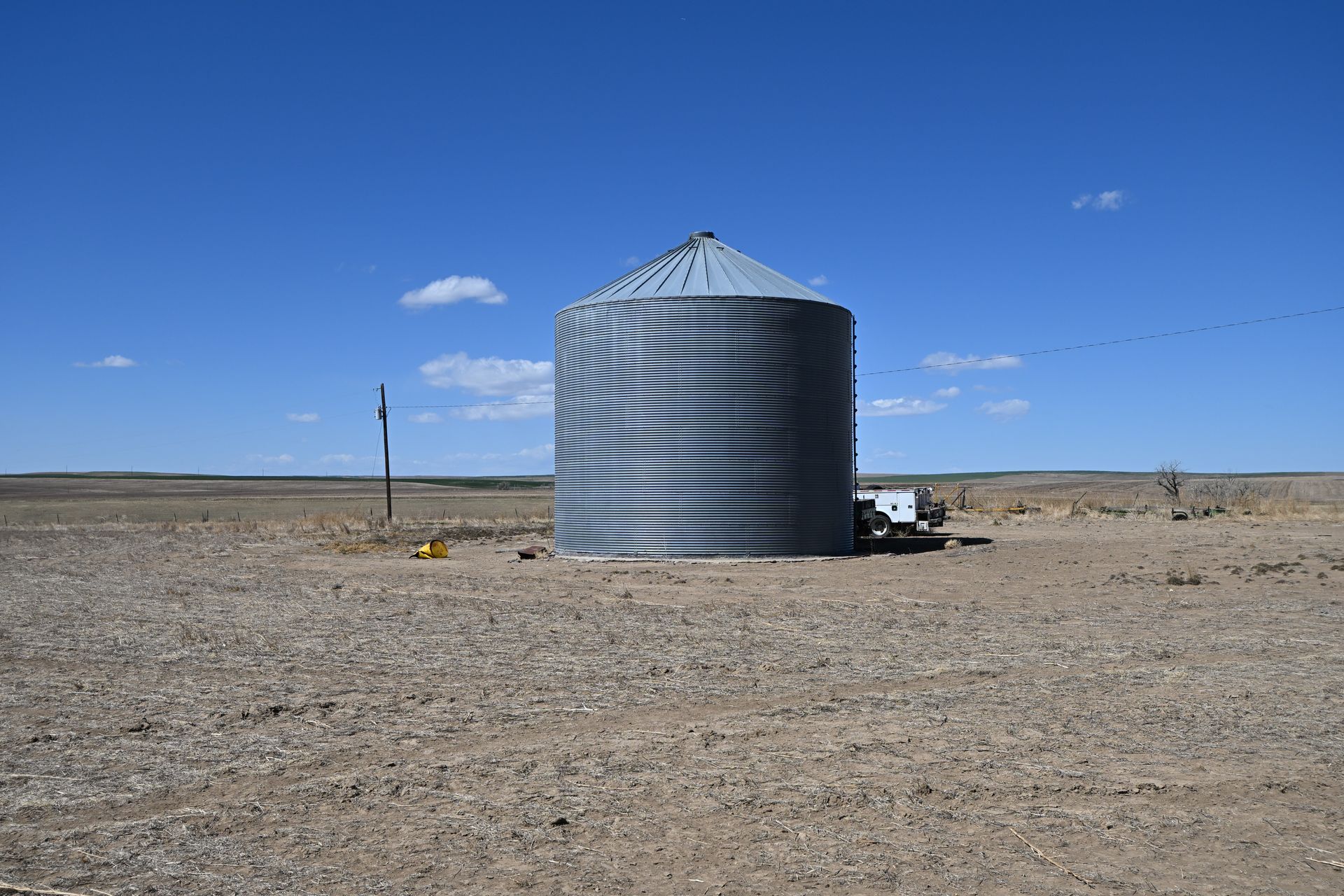Large metal grain silo in a barren field under a clear blue sky