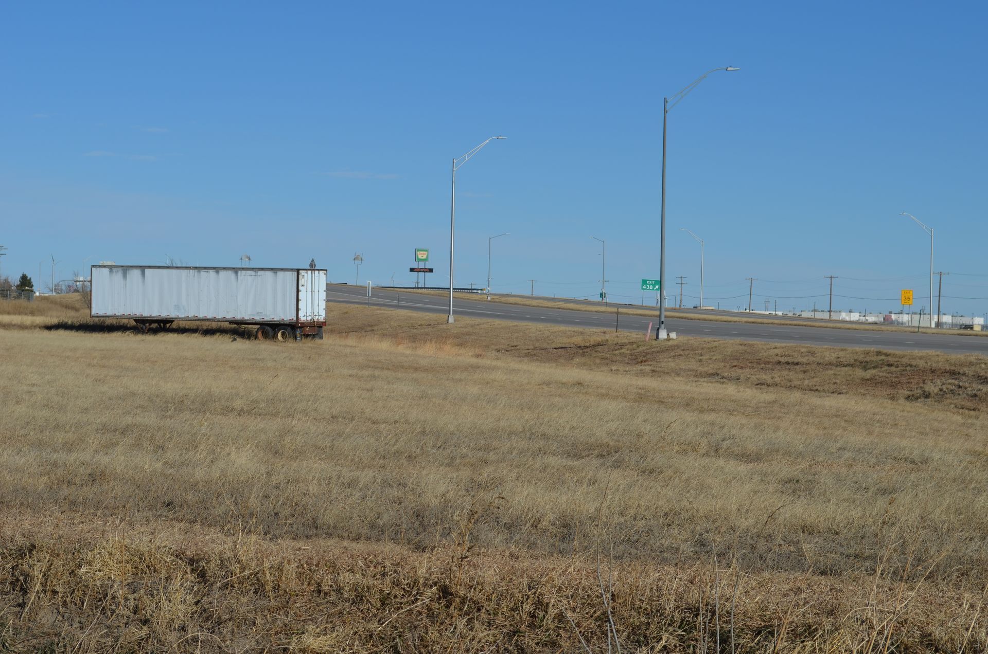 White trailer in a field of dry grass next to a highway on a sunny day.