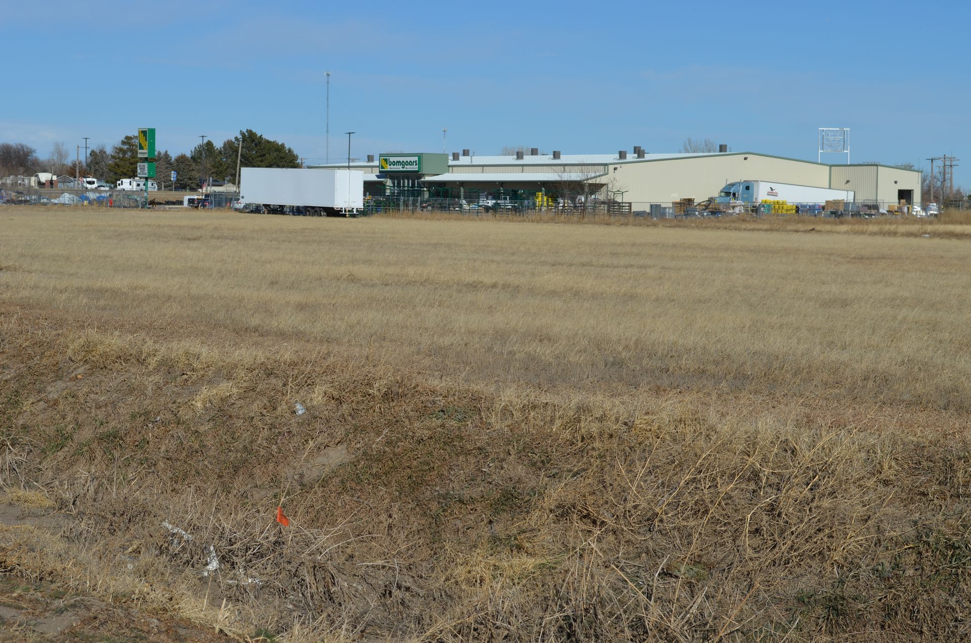 Field of dry grass with a large industrial building in the background on a sunny day.